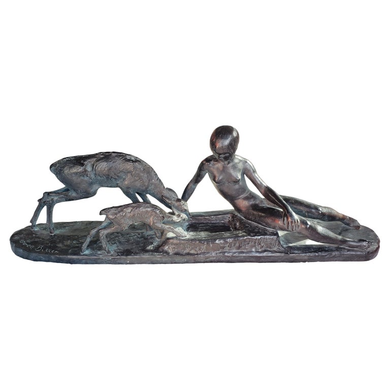 A fine signed sculpture of a naked young woman seated on a rectangular shaped self plinth and feeding a mother deer and its fawn. The bare chested female figure in a semi reclining pose is portrayed with a mother deer fawn drinking out of a trough