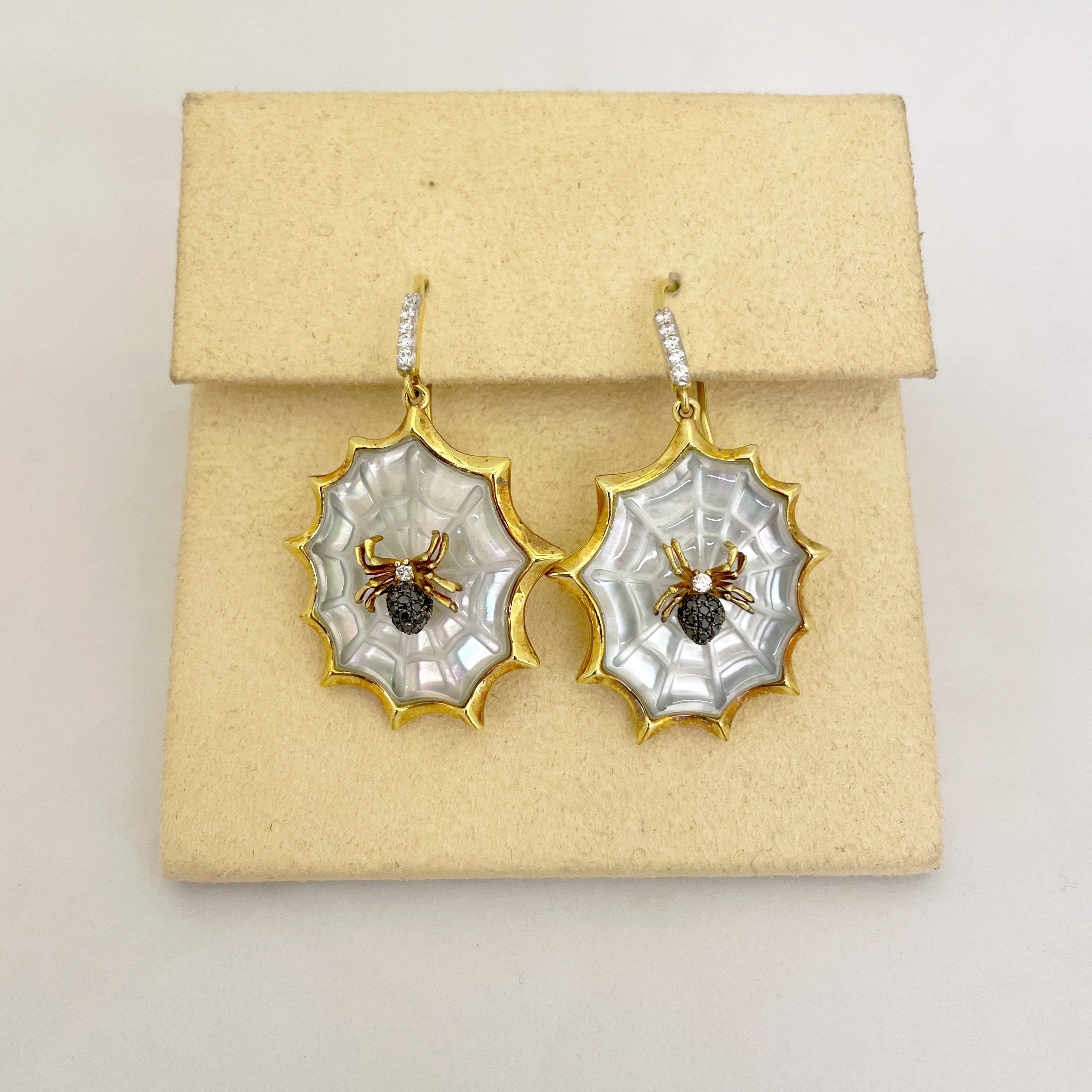 Designed by Asch Grossbardt, these unique 18 karat yellow gold earrings are crafted as bejeweled spiders sitting on their web. Hand carved mother of pearl forms the web for the black and white diamond spiders. Round diamonds accent the gold hanging