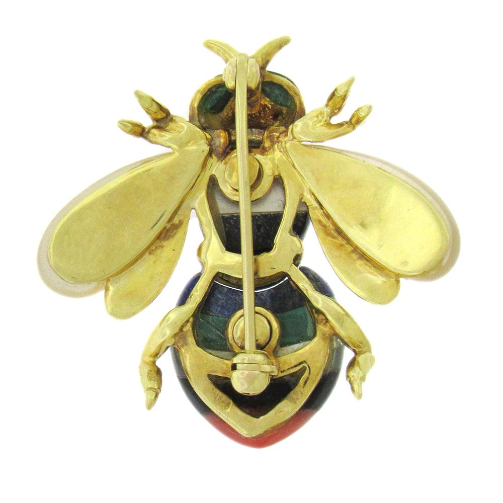 A colorful gem-inlay bee pin from, circa 1970's, in 14K gold from Asch Grossbardt, set with incised mother-of-pearl wings, lapis, onyx, malachite and a coral tail, with green malachite eyes. The pin measures  1-1/4