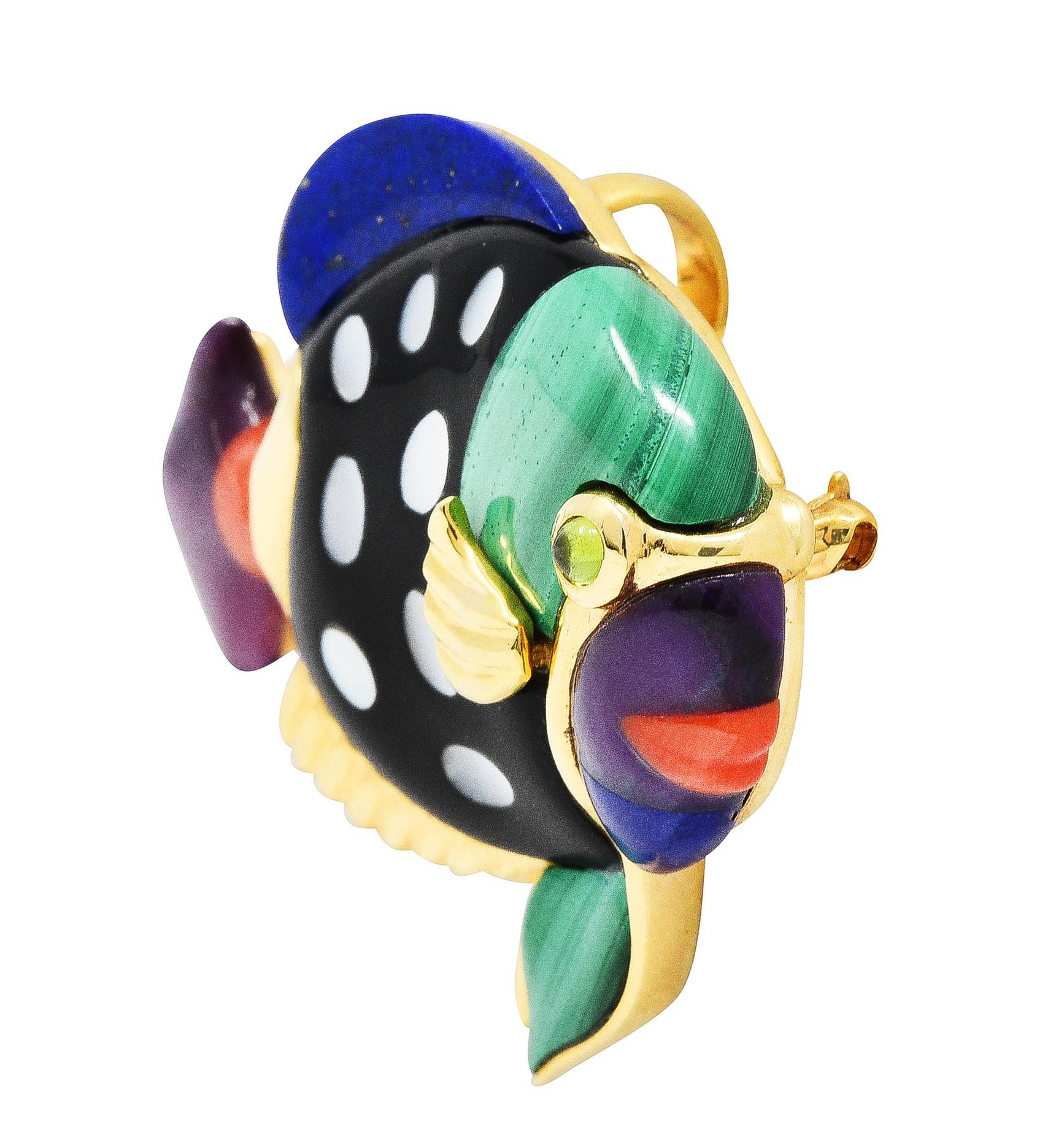 Pendant brooch designed as stylized fish with high polished ridged gold fins

Featuring lapis lazuli, coral, amethyst, onyx, malachite, and mother-of-pearl - flushly inlaid

With a bezel set 2.5 mm round peridot cabochon eye

Completed by pin stem