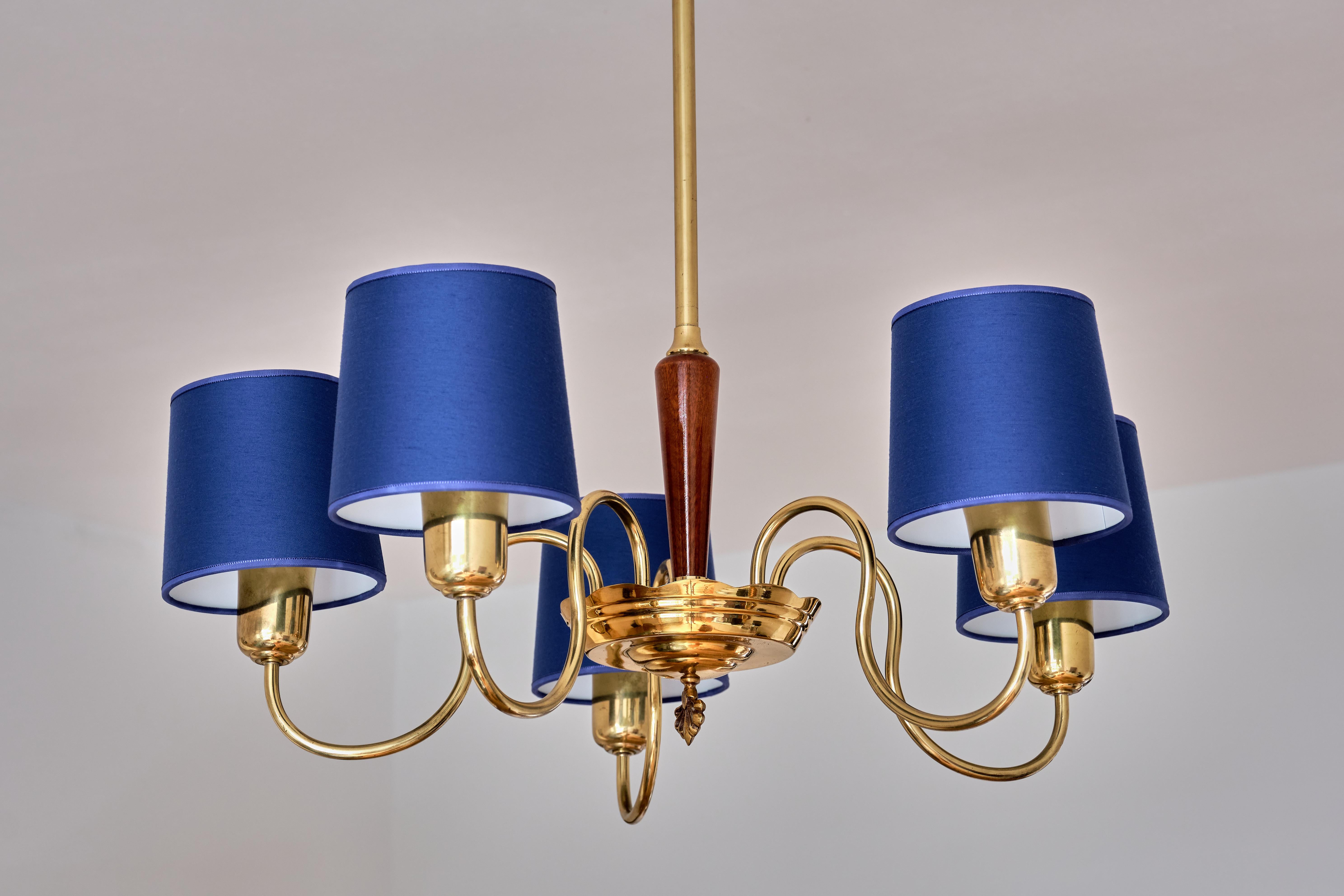 This elegant brass chandelier was produced by ASEA Belysning in Sweden in the 1940s. The brass stem leading to a wooden column in lacquered elm and a brass receiver bow with a crown finial detail. The five arms and tubular lamp holders are in brass