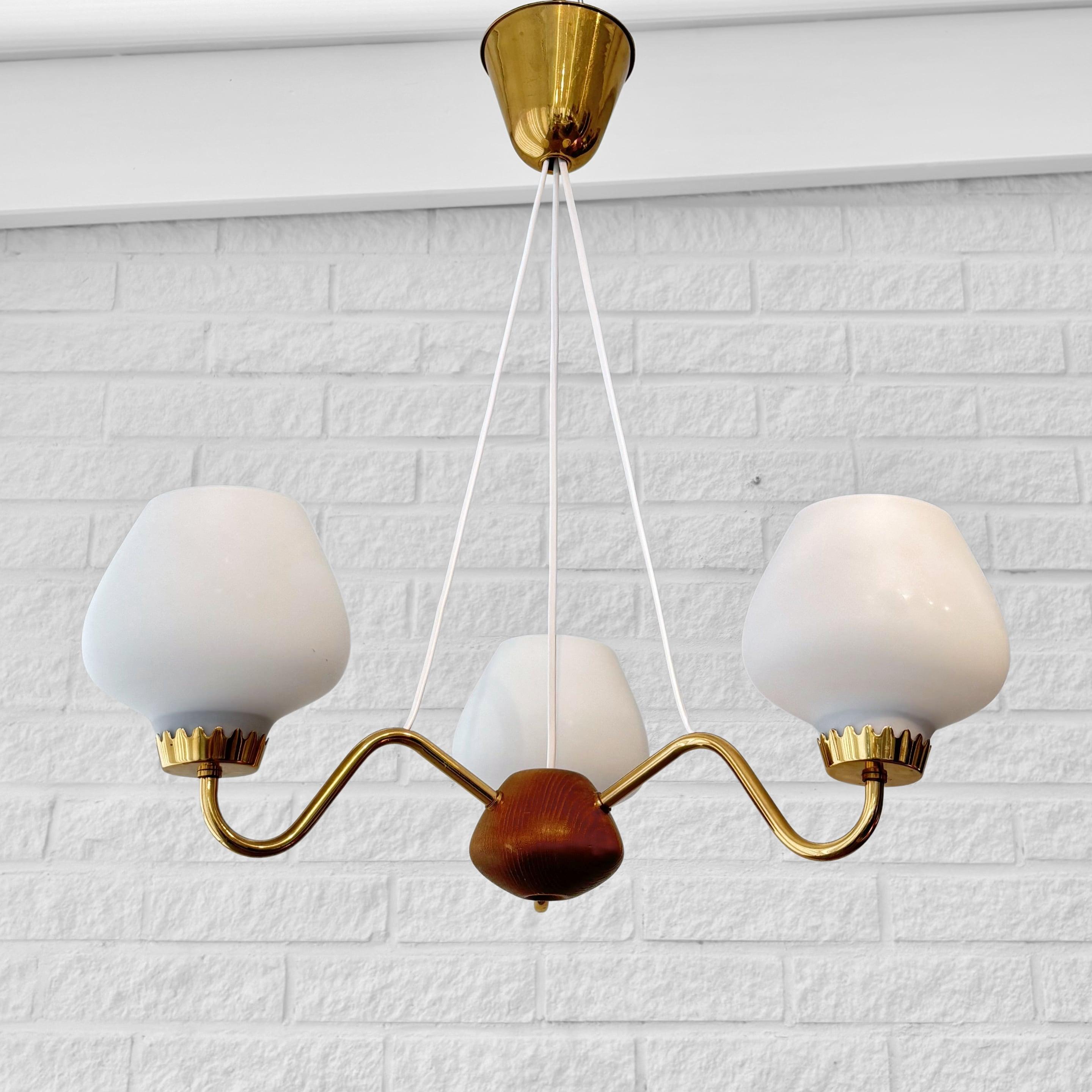 A beautiful vintage chandelier produced by the renowned Swedish lighting manufacturer ASEA Belysning in the 1950s. Crafted from brass, it features three gracefully curved arms, each holding a bell-shaped glass shade. The arms are anchored by a