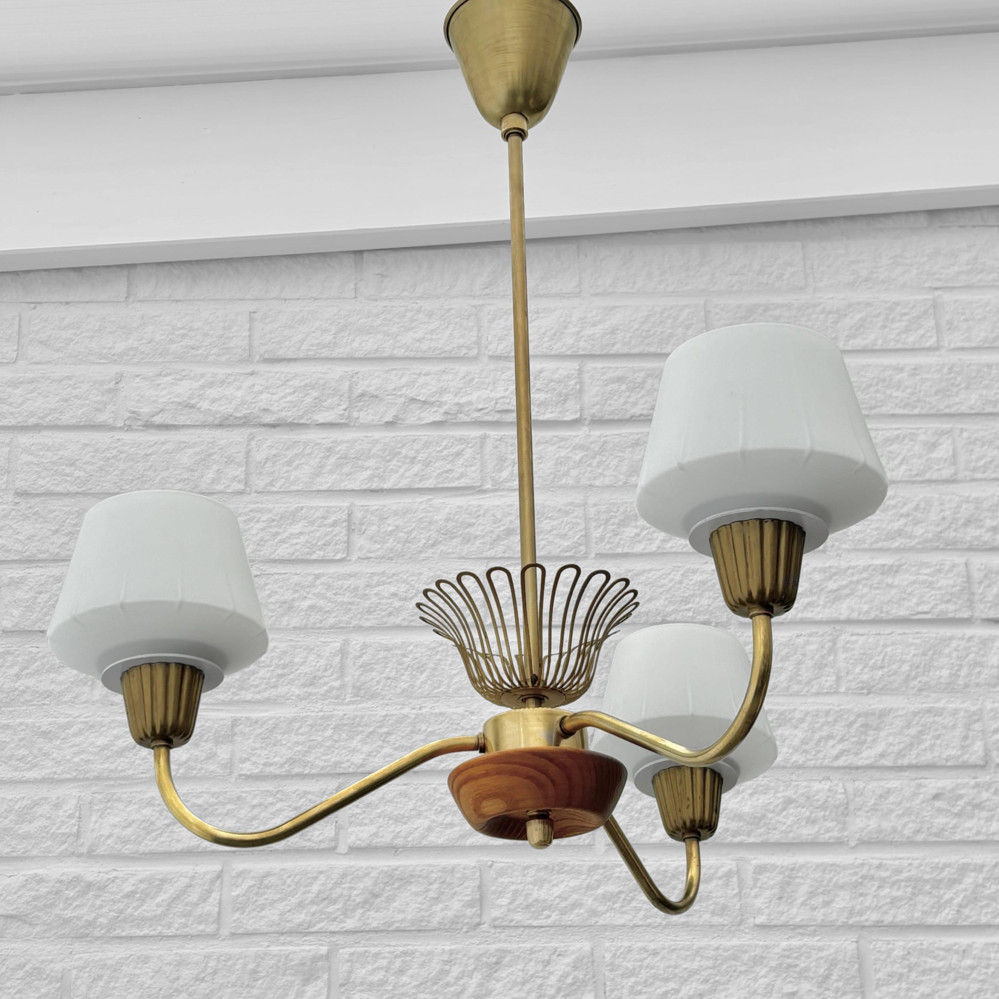 Un lampadario modernista prodotto dal produttore di illuminazione svedese ASEA Belysning negli anni '50. Realizzato in legno massiccio di quercia e ottone, presenta tre bracci curvi che sorreggono paralumi in vetro bianco e include il suo originale