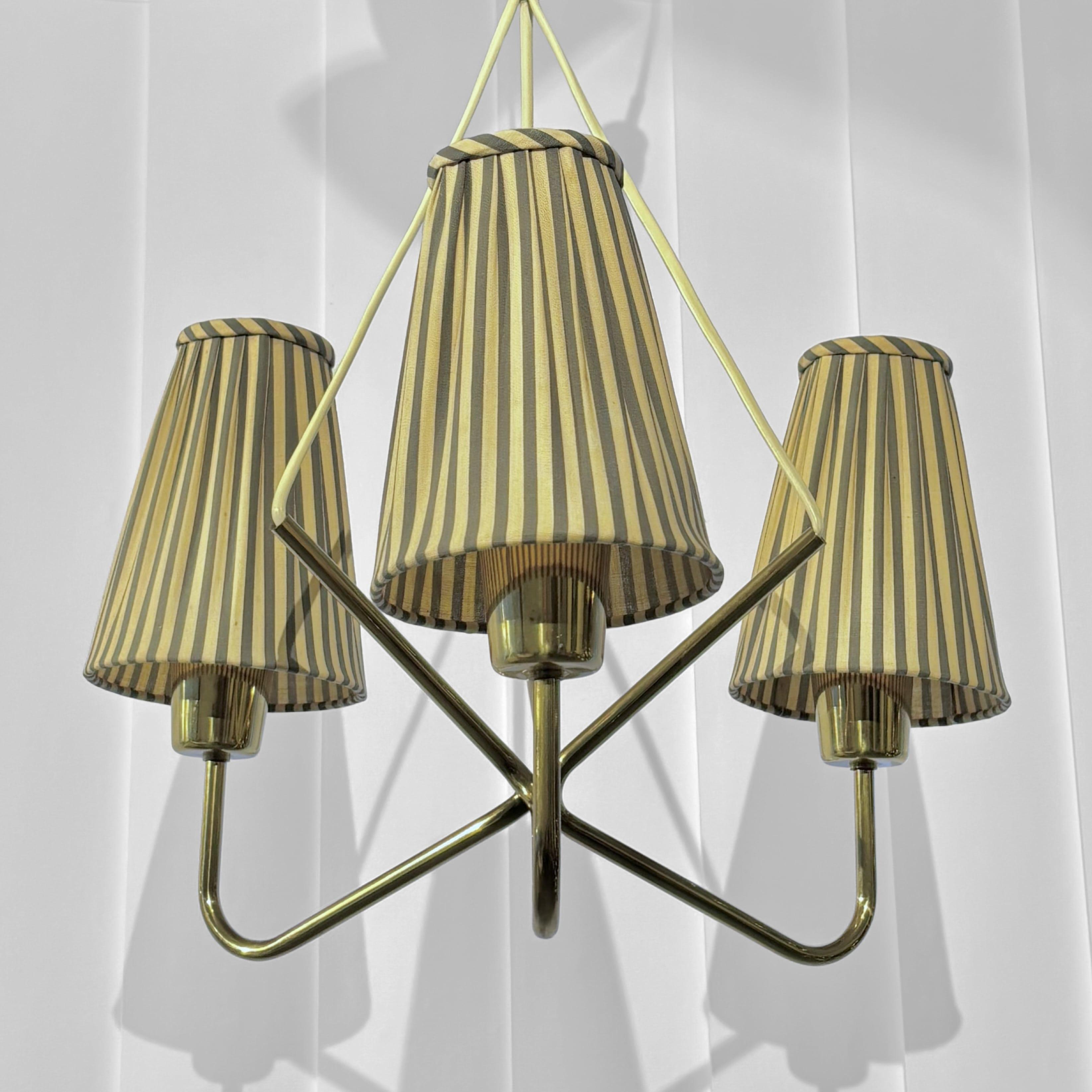 A modernist chandelier produced by the renowned Swedish lighting manufacturer ASEA Belysning in the 1950s. It features a geometric design crafted from brass pipes arranged in a striking pattern. Three arms, each holding a conical lampshade