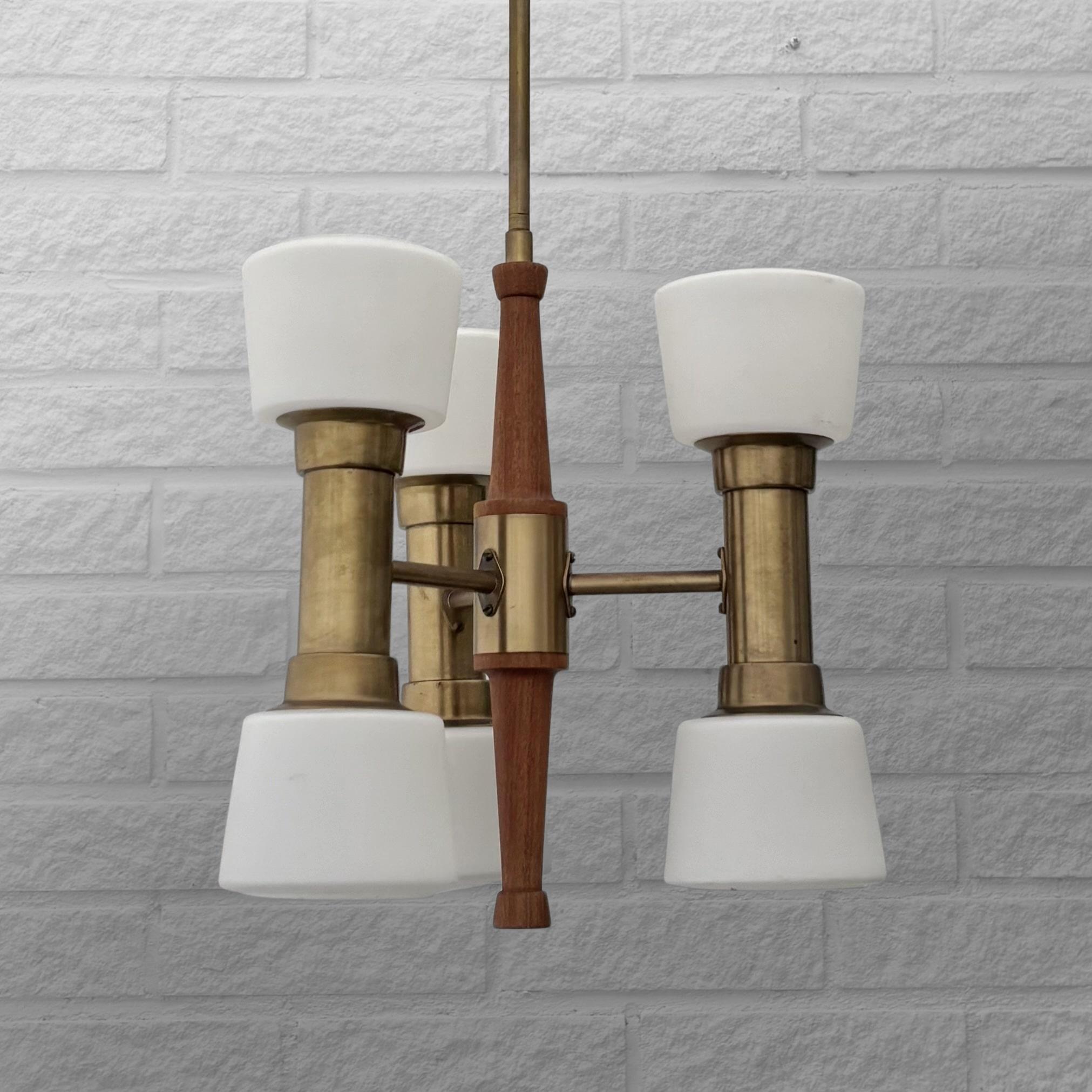 A modernist chandelier produced by the Swedish lighting manufacturer ASEA Belysning in the 1950s. Crafted from solid teak and brass, it features six arms holding white glass lampshades and includes its original dome-shaped ceiling canopy. The