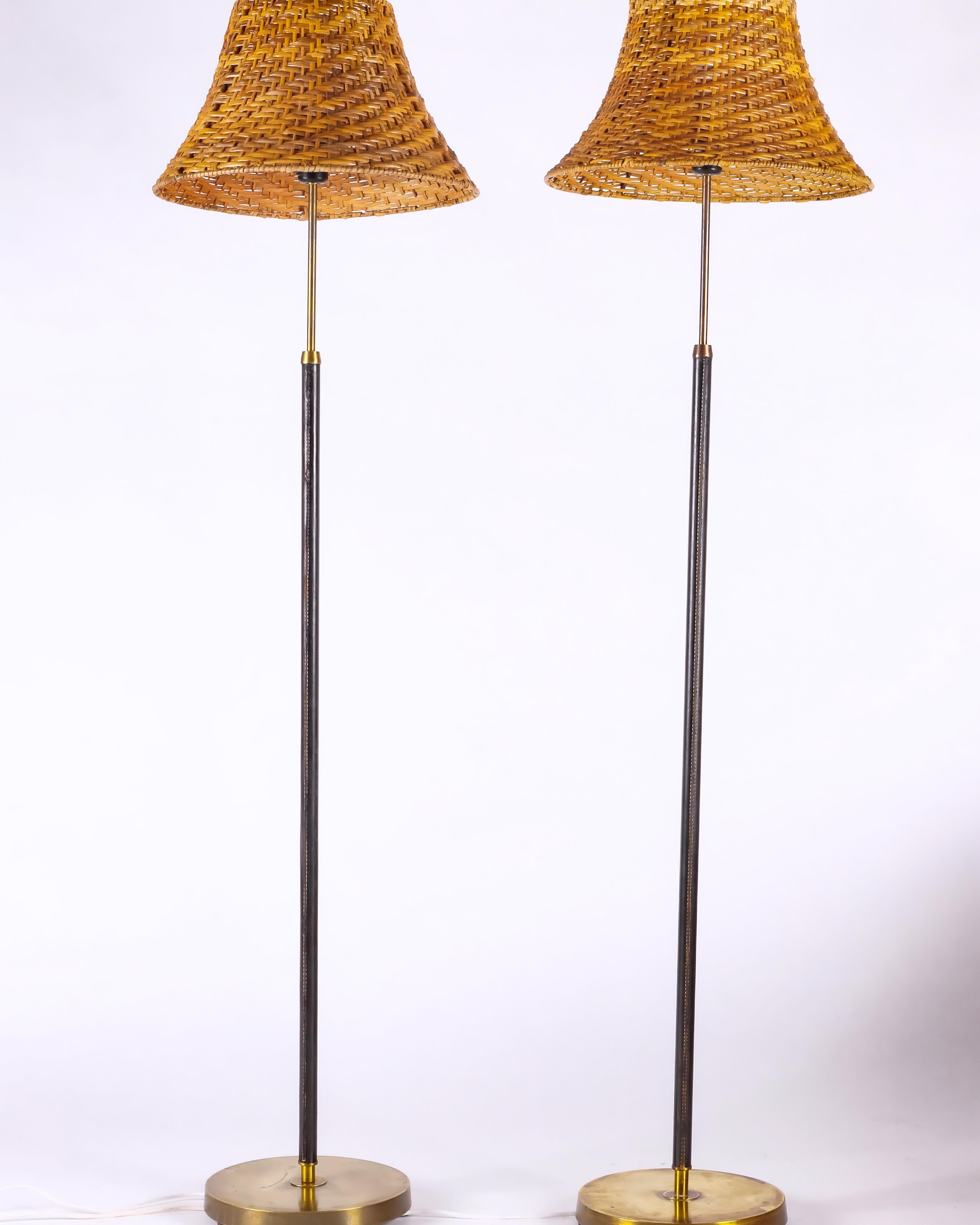 Standing pair of leather wrapped brass lamps, imported from Sweden and rewired for US. Rattan shades included. Age-appropriate patina and signs of use to the brass and the leather elements. Not adjustable. Sold as pair.