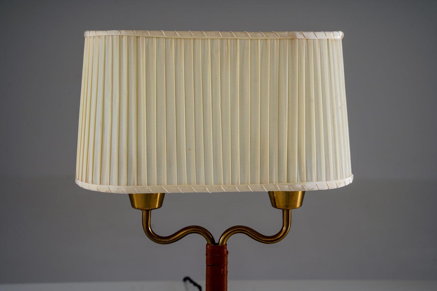 Lampe de table suédoise raffinée d'ASEA, dotée d'un double bras en laiton, d'une tige centrale enveloppée de cuir et d'une solide base rectangulaire. Elle conserve son abat-jour en tissu plissé d'origine, qui met en valeur le caractère