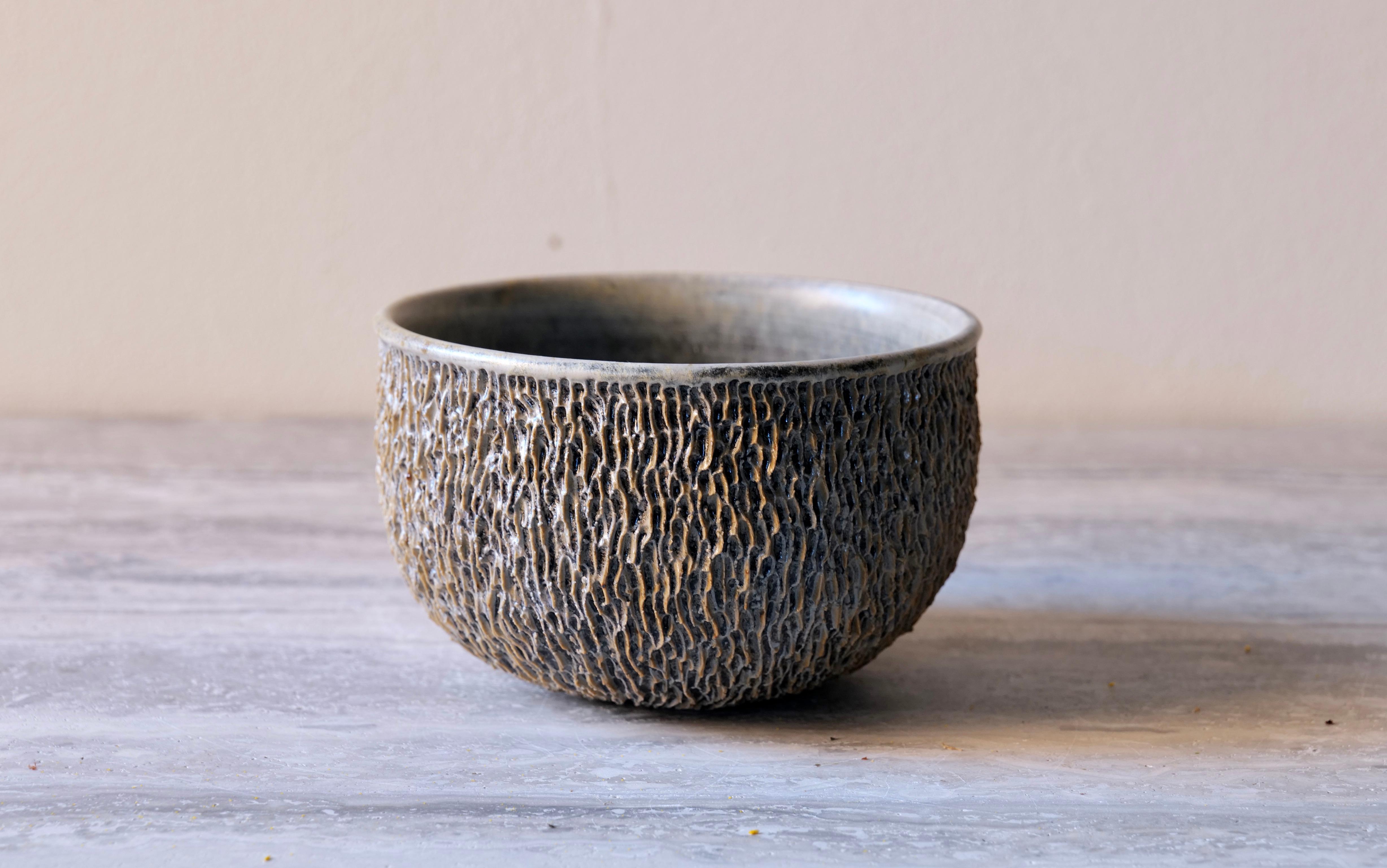 Die Ash Carved Small Bowl verkörpert eine raffinierte Balance zwischen Textur, Farbe und Form. Von Hand getrieben und kunstvoll geschnitzt, weist das Äußere eine lineare, rindenartige Textur auf, die an verwittertes Holz oder Korallen erinnert. Die