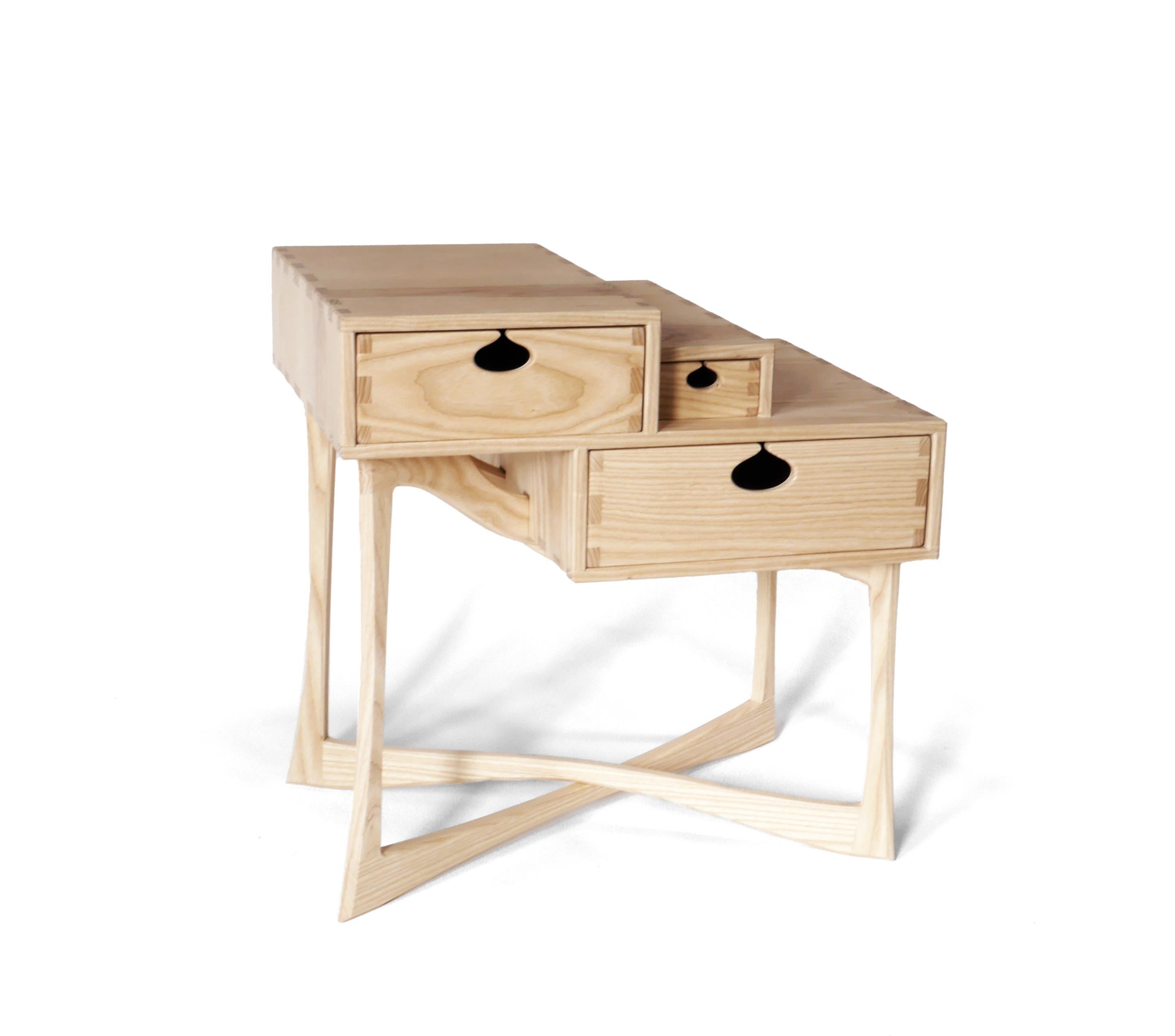 La table d'appoint charismatique Coriolis est fabriquée en frêne blanc massif et comporte trois tiroirs montés sur des glissières en bois dans des boîtes à tiroirs traditionnelles. Il est construit avec des menuiseries apparentes qui ont été