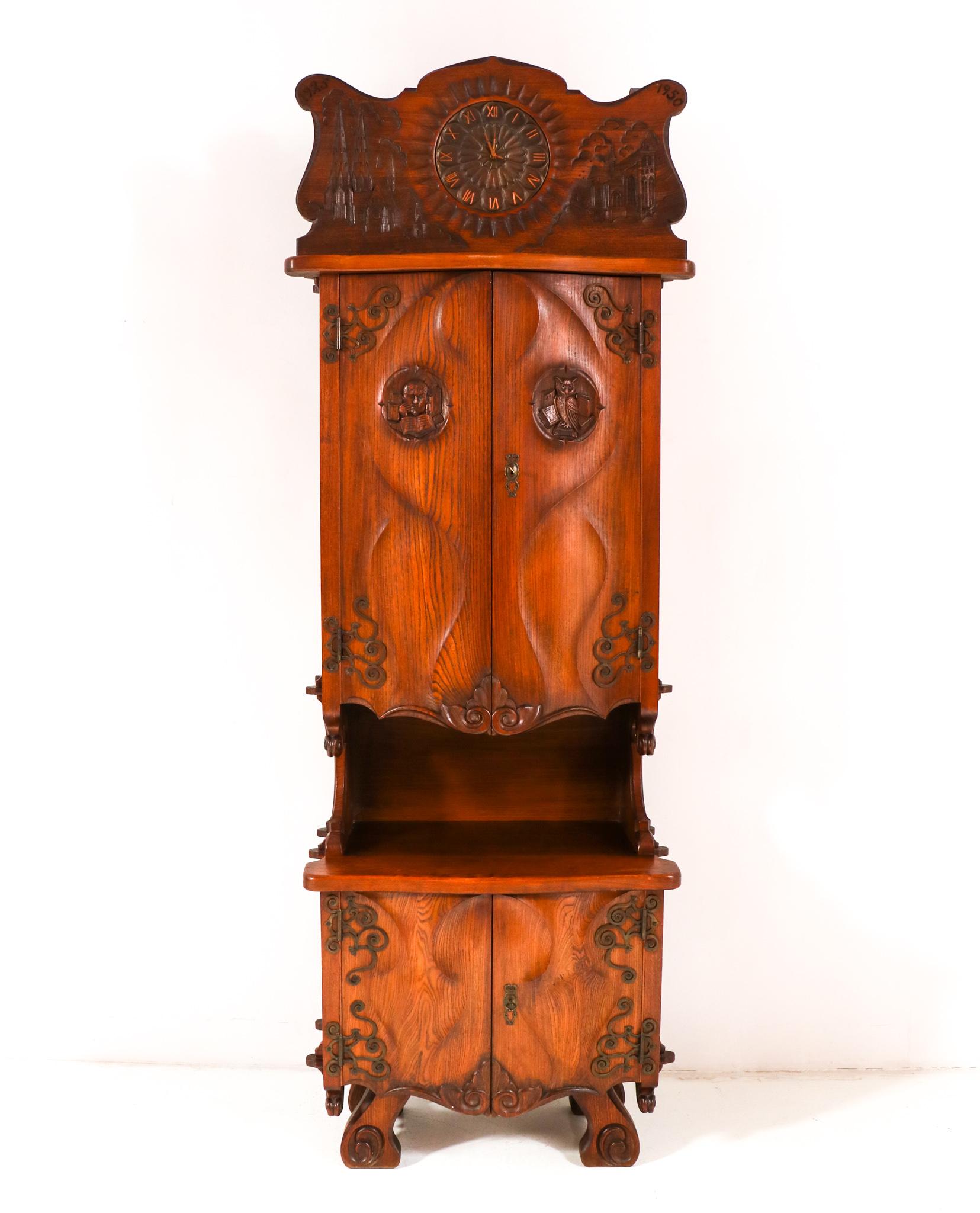 Magnificent and ultra rare Gothic Revival cupboard.
Striking Dutch design from the 1950s.
Solid ash with a integrated patinated brass clock and patinated wrought iron hinges.
Decorated with original hand-crafted elements like churches and an owl