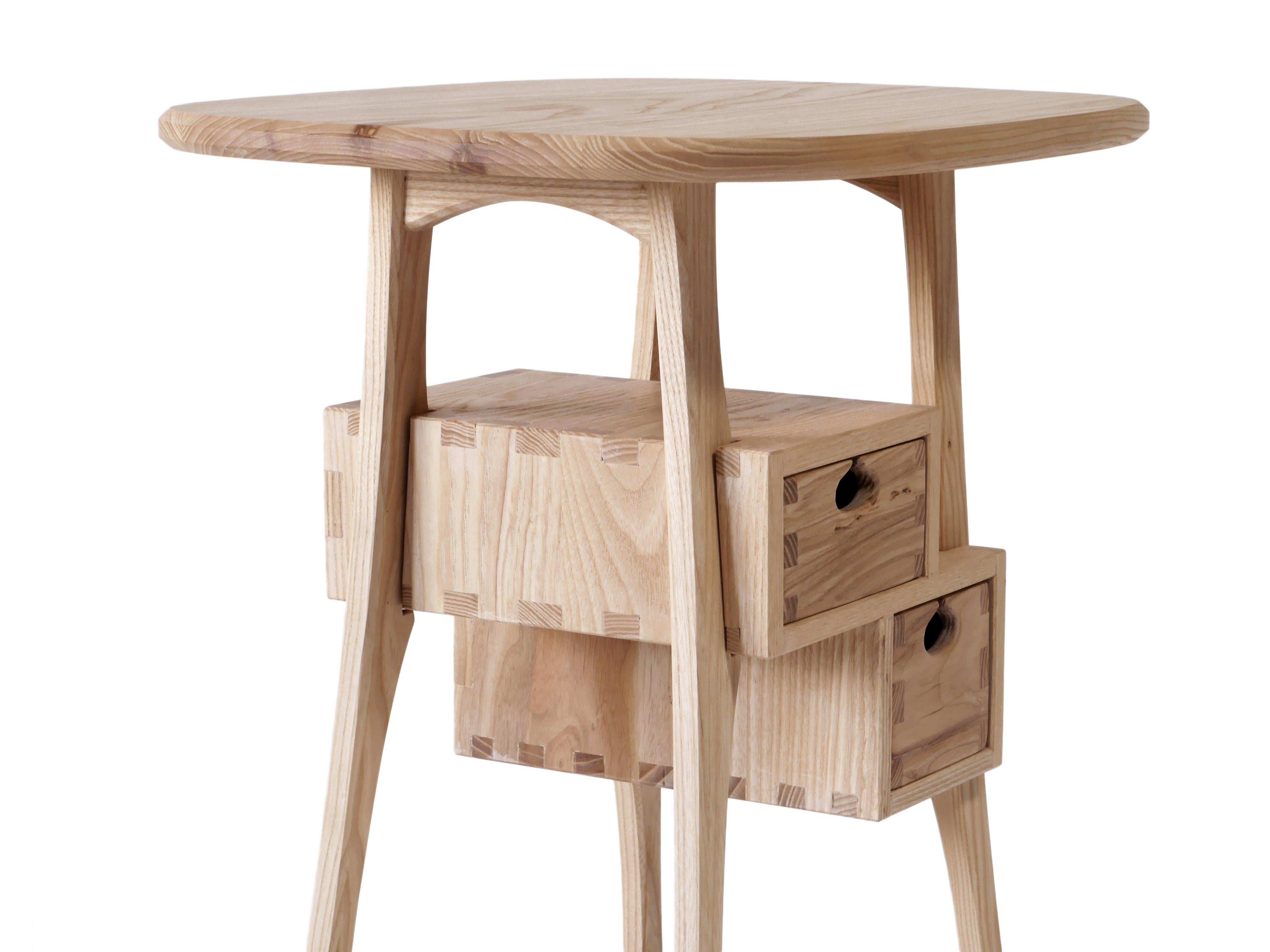 La table d'appoint Haar, très ludique, est fabriquée en frêne blanc massif et comporte deux tiroirs montés sur des glissières en bois dans des boîtes à tiroirs traditionnelles. Il est construit avec des menuiseries apparentes qui ont été
