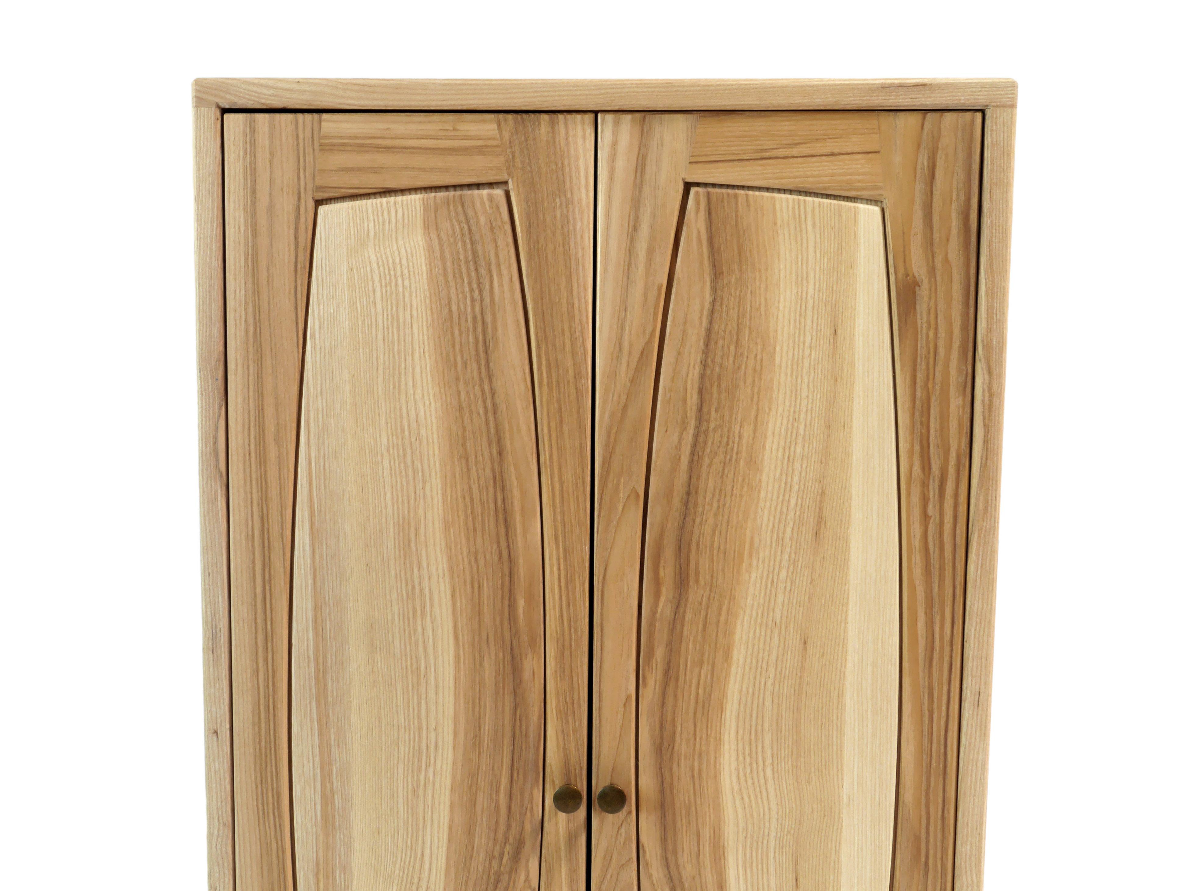 The stately Vespers Side Cabinet is built of solid ash hardwood with a black walnut stand. Its two doors are made with curved frame and raised panel construction adding playfulness to a traditional form.  It has a single solid wood adjustable shelf