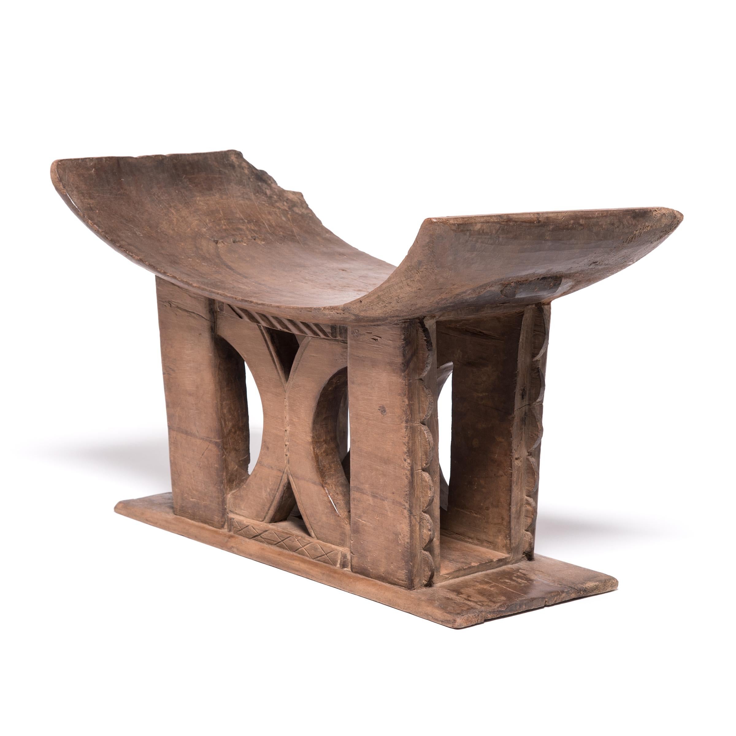 In traditional Ashanti culture, stools indicated power, status, and lines of succession. The flat base, curved seat, and ridged supports of this hand-carved stool reference the Ashanti King Stool. The central symbol is a simplified and turned