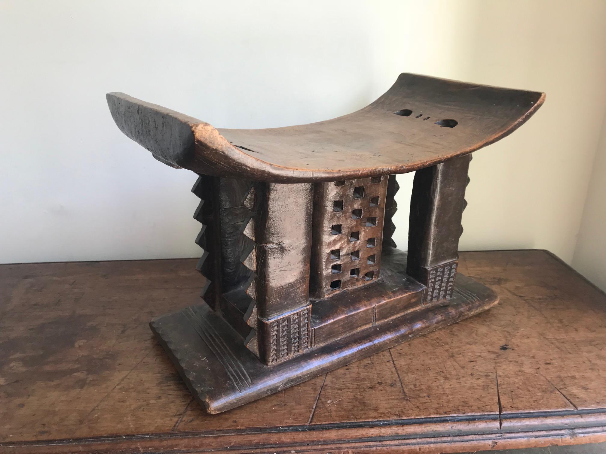 An Ashanti or Asante tribal stool. Carved from one piece of wood, this example has typical Ashanti geometric carvings with a central pierced support column. It has suffered one break, which is a good feature as shows it was used and not made for the