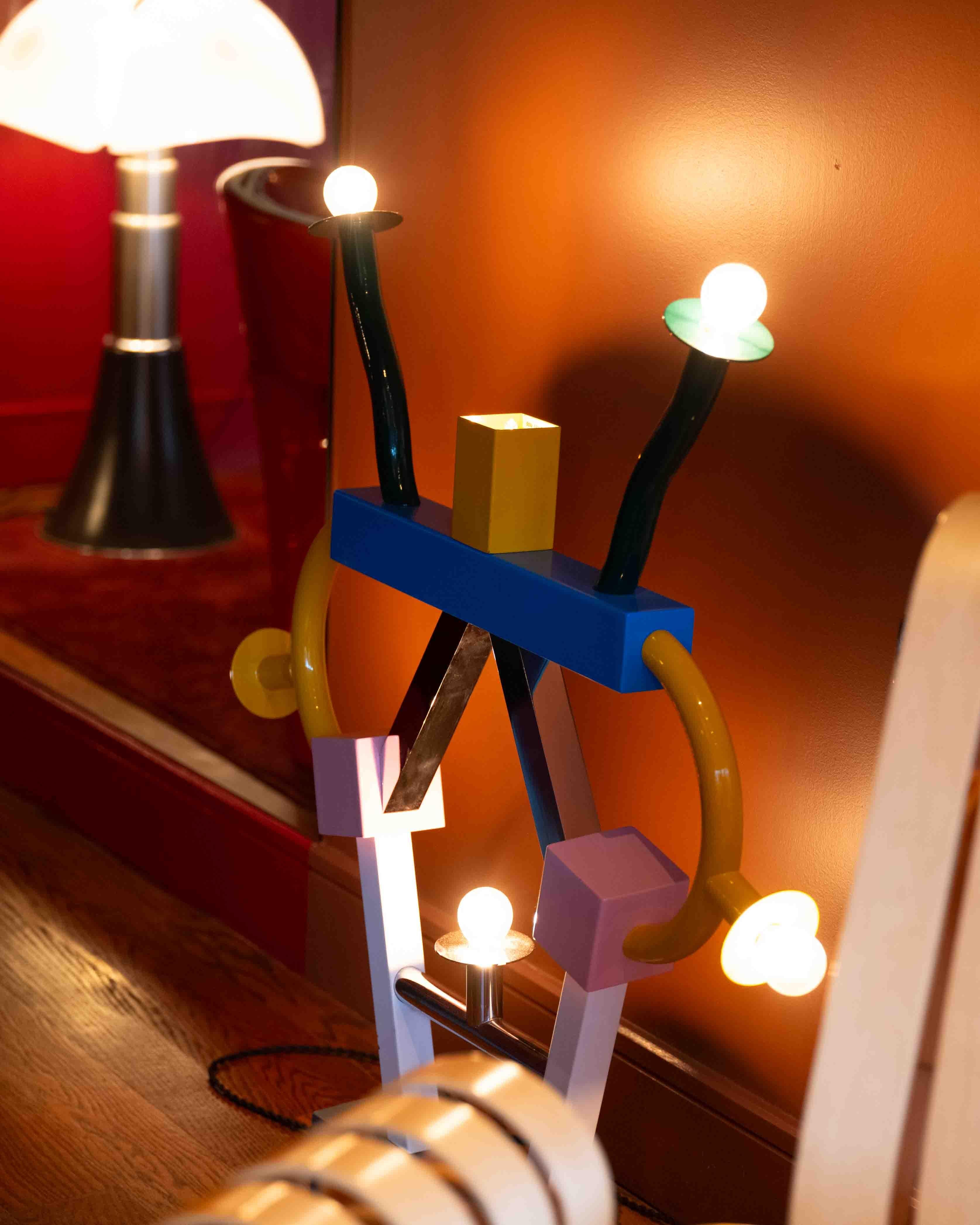 La lámpara de sobremesa Ashoka, diseñada por Ettore Sottsass para Memphis Milano, toma su nombre del emperador del Imperio Maurya. La lámpara está fabricada en materiales esmaltados y cromados, y presenta diversas formas geométricas. 