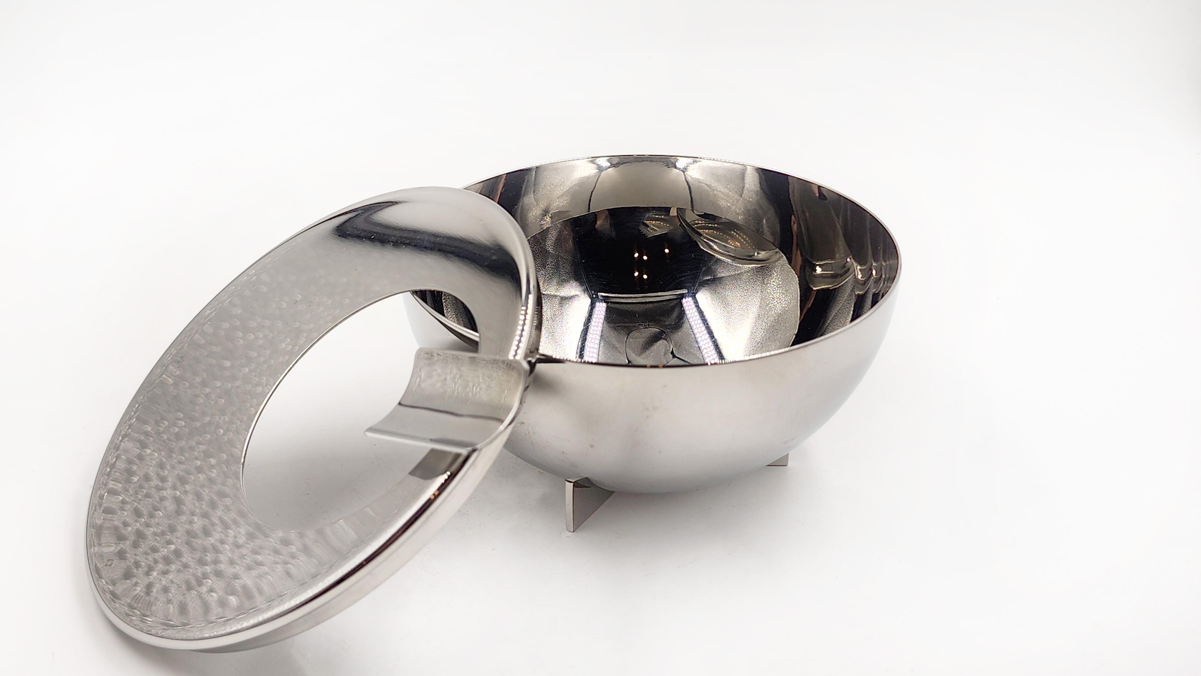 Posacenere di Marianne Brandt per Alessi
Posacenere disegnato da Marianne Brandt per Alessi. Questo posacenere ha una forma emisferica con un coperchio piatto e circolare che incorpora un'apertura ovale per la raccolta della cenere. Dal coperchio