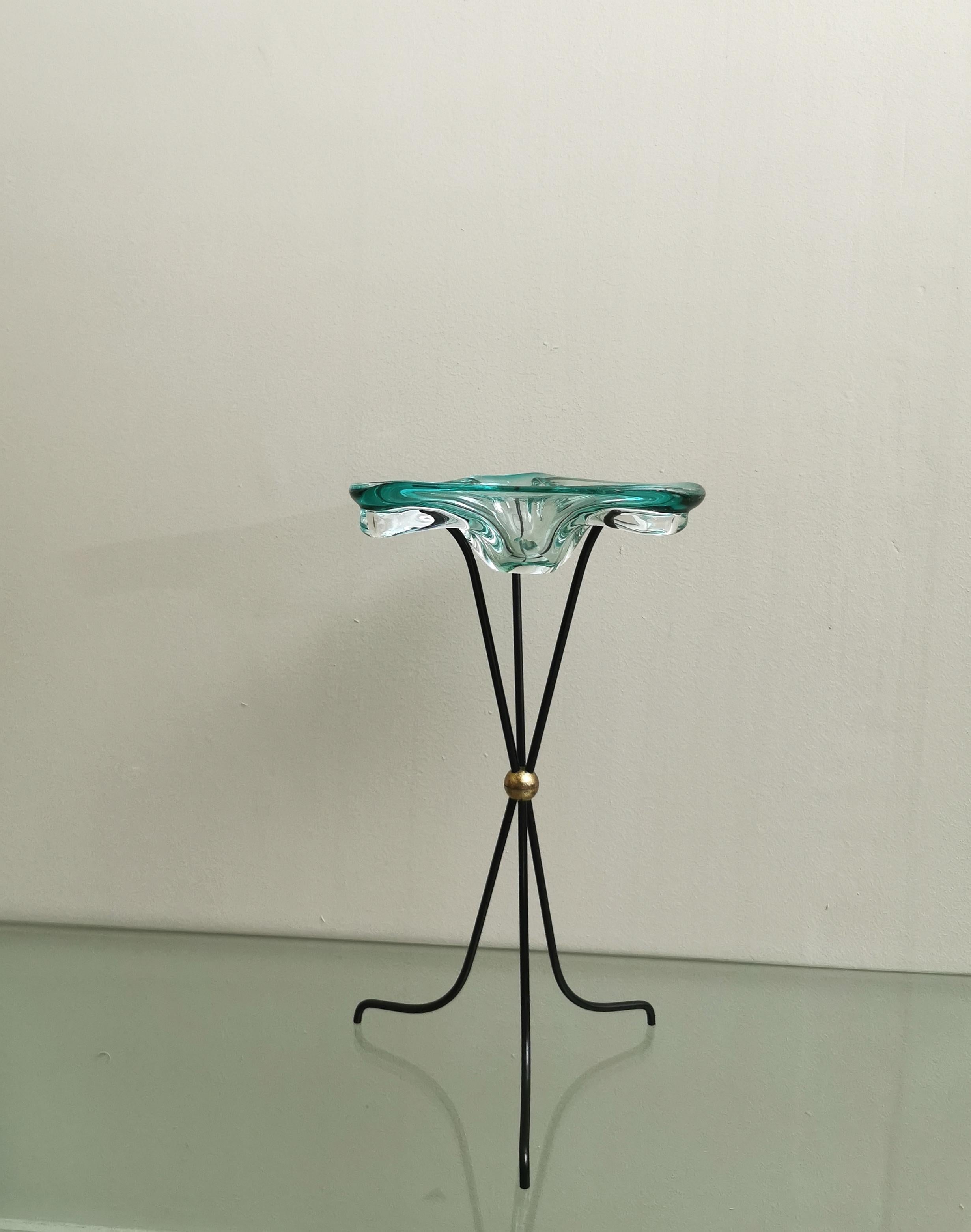 Ashtray designed by the Italian designer Albano Poli and produced in the 70s. The triangular shaped ashtray with rounded corners is in handmade Murano glass in the shade of nile green with a 3-foot structure in black enamelled metal with brass