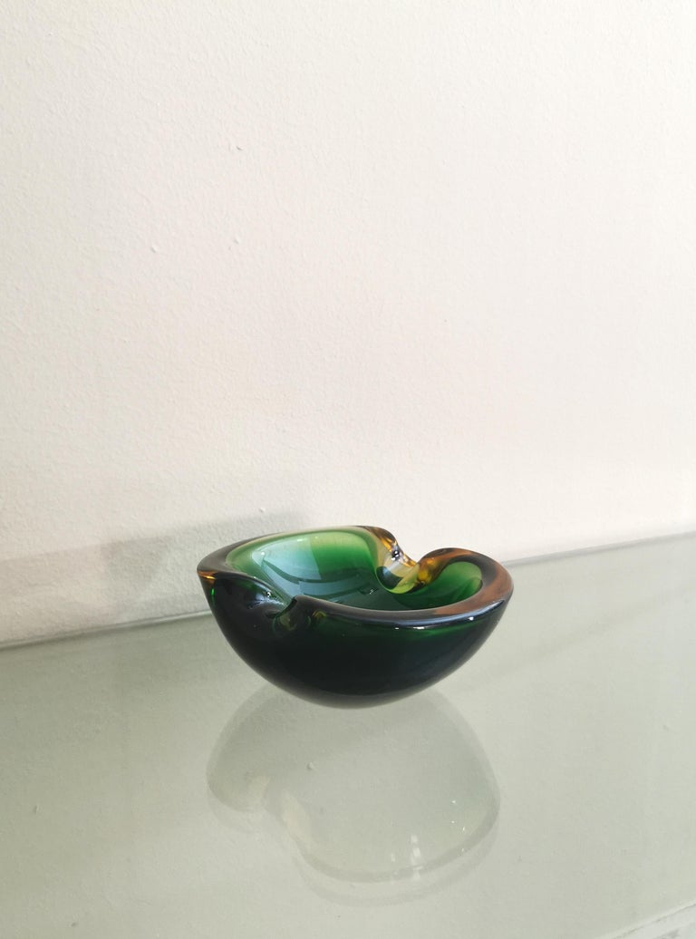 Ashtray with sinuous lines produced in Italy in the 70s by the Italian designer Flavio Poli.
The ashtray was made of Murano glass, in the shades of bottle green and amber with the famous 