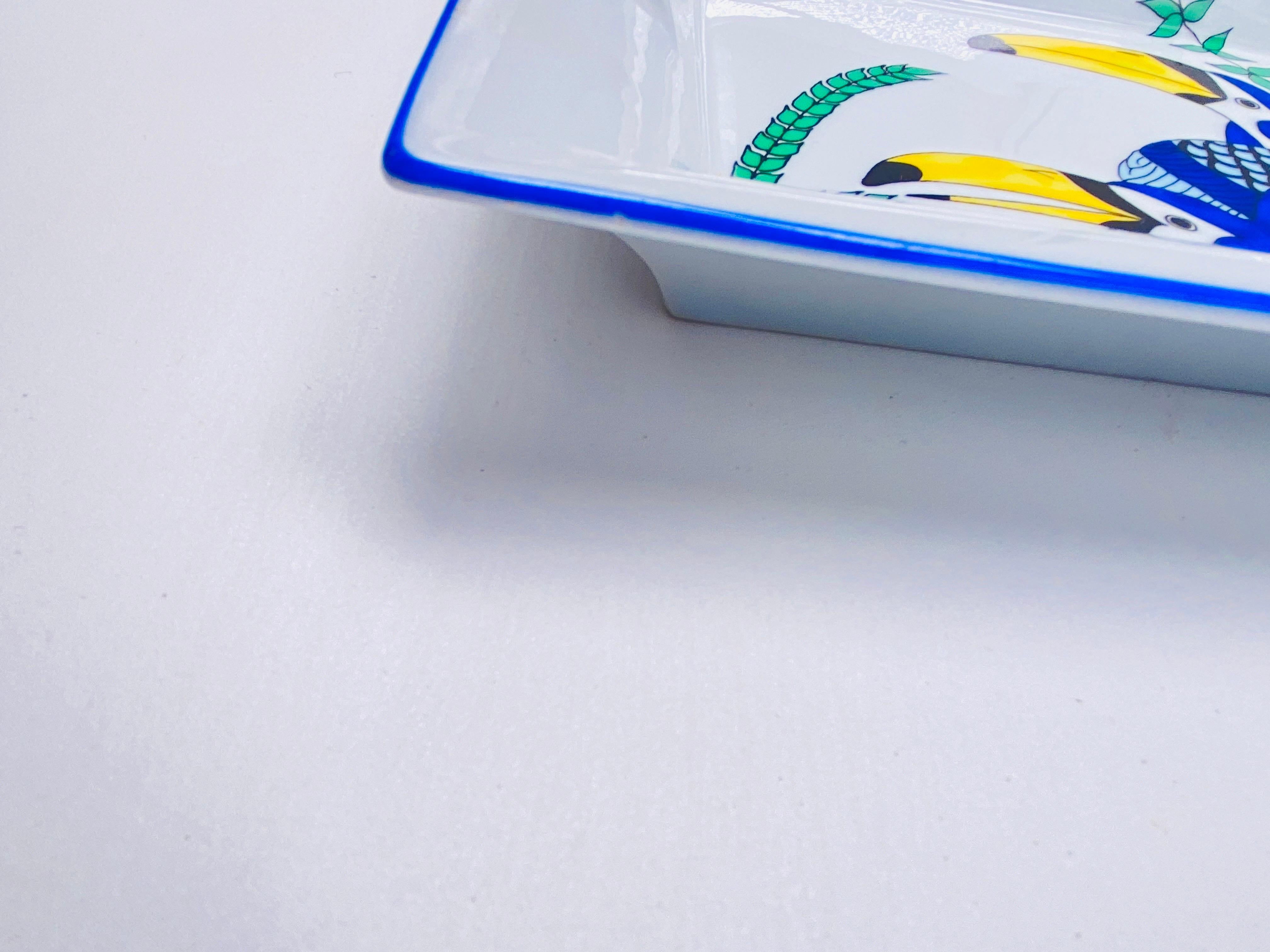 These handsome hand-painted Limoges porcelain ashtray is in a vibrant blue and yellow color with gilded accents and abirdr design. This piece is by Deshoulières Limoges, made for a company named Somangest, and signed by artist Sophie d'E.
It is a