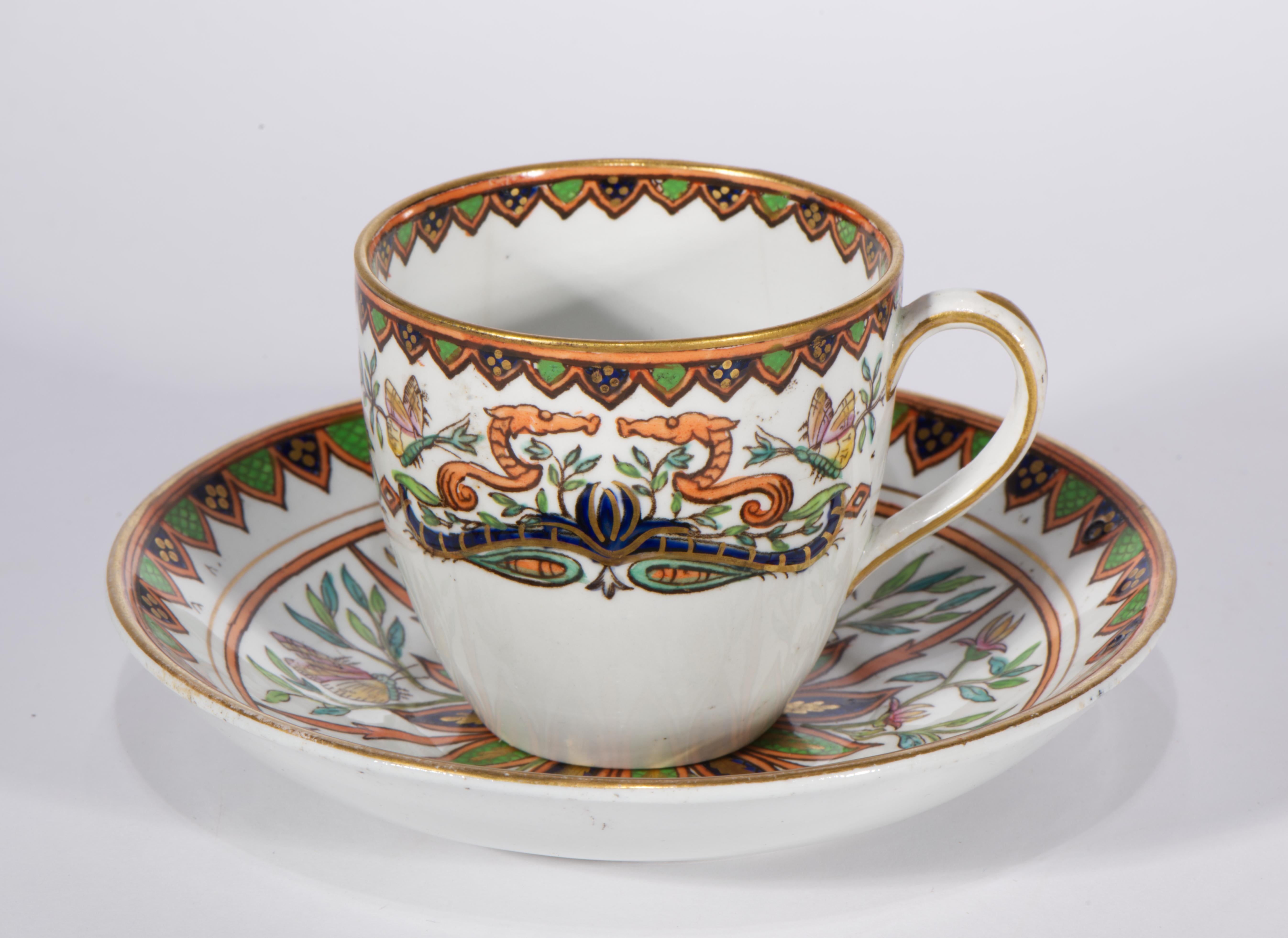  Antikes Set aus Tasse und Untertasse aus Eisenstein mit handgemaltem Dekor mit abstrakten geometrischen Bordüren auf den Rändern in Blau, Grün, Orange und Gold sowie einem Dekor im Stil des Arts and Crafts mit blühenden Zweigen und Schmetterlingen