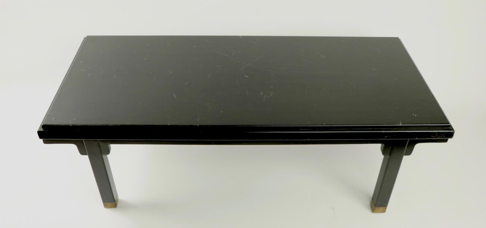 Diminutive and graphic Asia Modern coffee table having all-over black finish and brass CAP feet. The finish shows cosmetic wear, light scratching and signs of age and use. Manufacture attributed to Baker Furniture, unsigned.