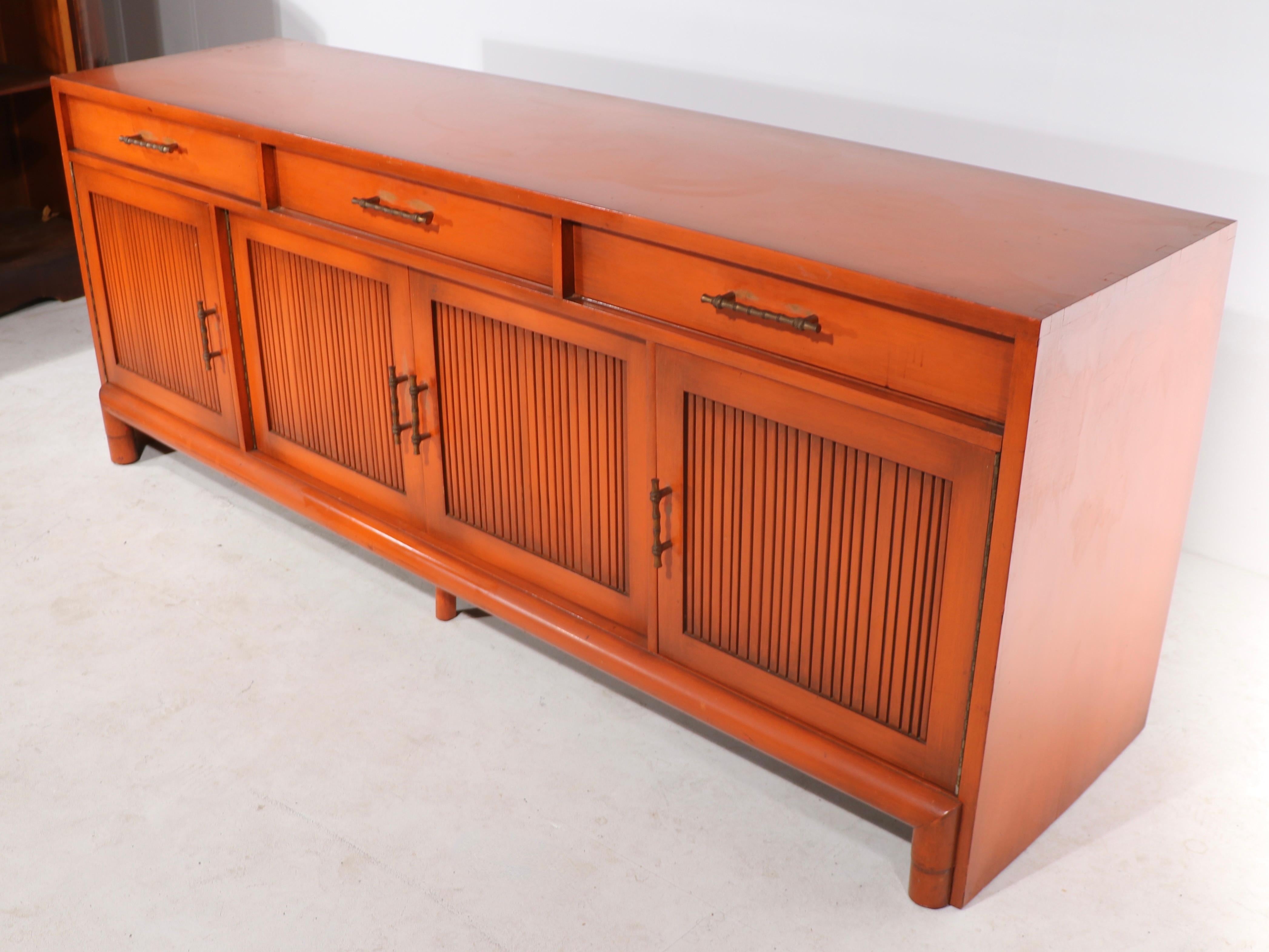 Large and impressive sideboard made by the Willett Furniture Company in the Chinese style, circa 1950/1960’s. The credenza is in an intriguing mandarin orange color lacquer finish and has ( later ) faux bamboo drawer pulls. The case features three