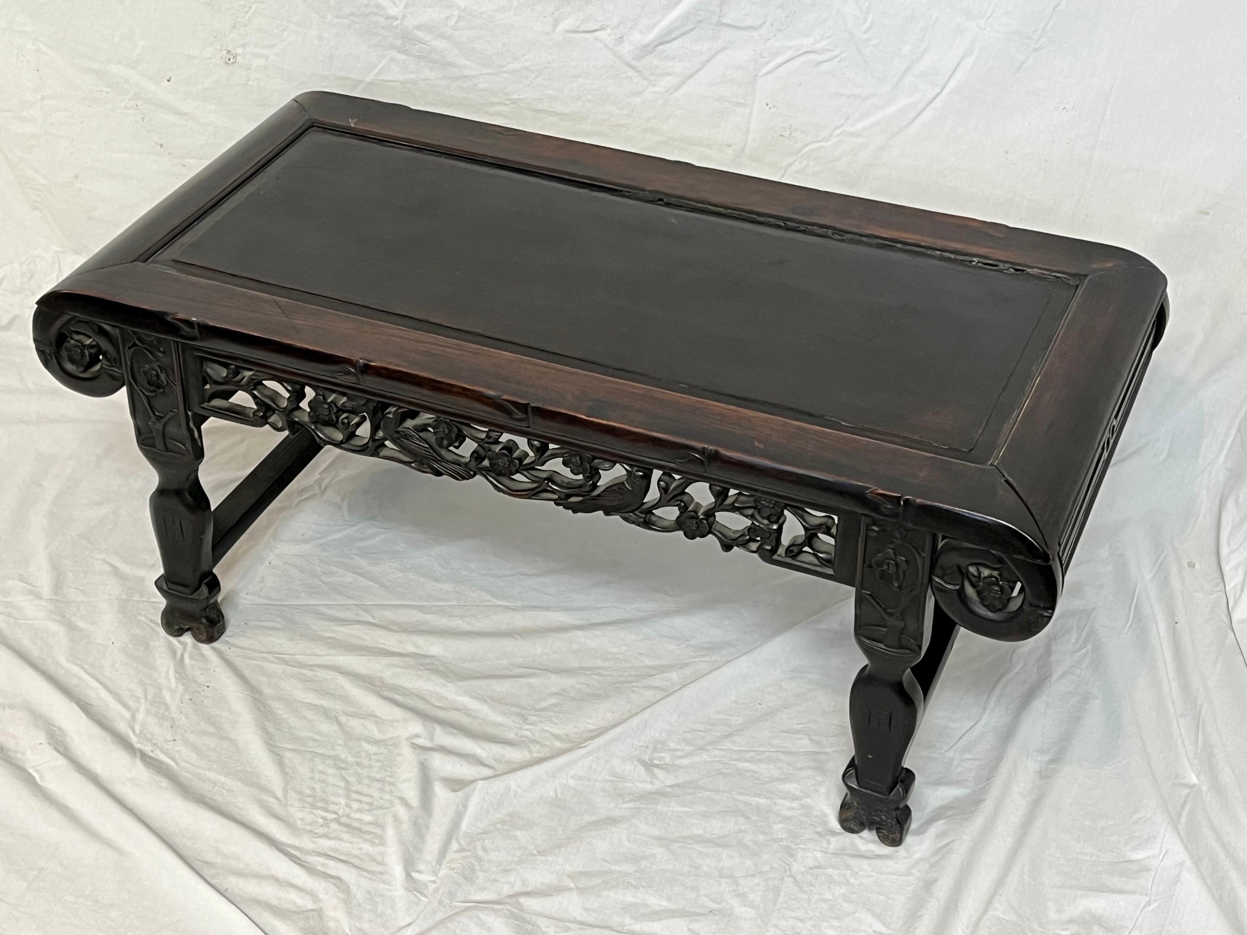A beautiful antique Asian low table with carved and pierced fretwork, rounded, scrolling corners, sitting low on four carved legs. This table features a deep, rich patina. The flora and fauna carved into the fretwork running the sides of the table