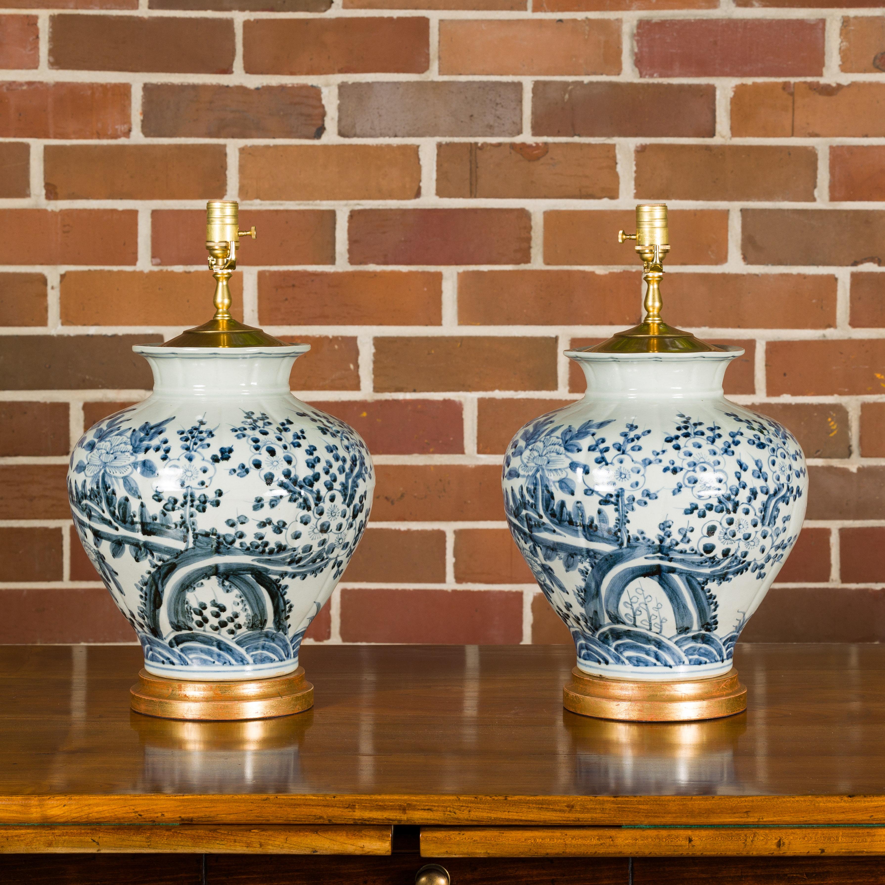 A pair of Asian blue and white porcelain vases with blooming tree and flying birds décor made into single light table lamps, wired for the USA and mounted on circular giltwood bases. Behold this exquisite pair of Asian blue and white porcelain