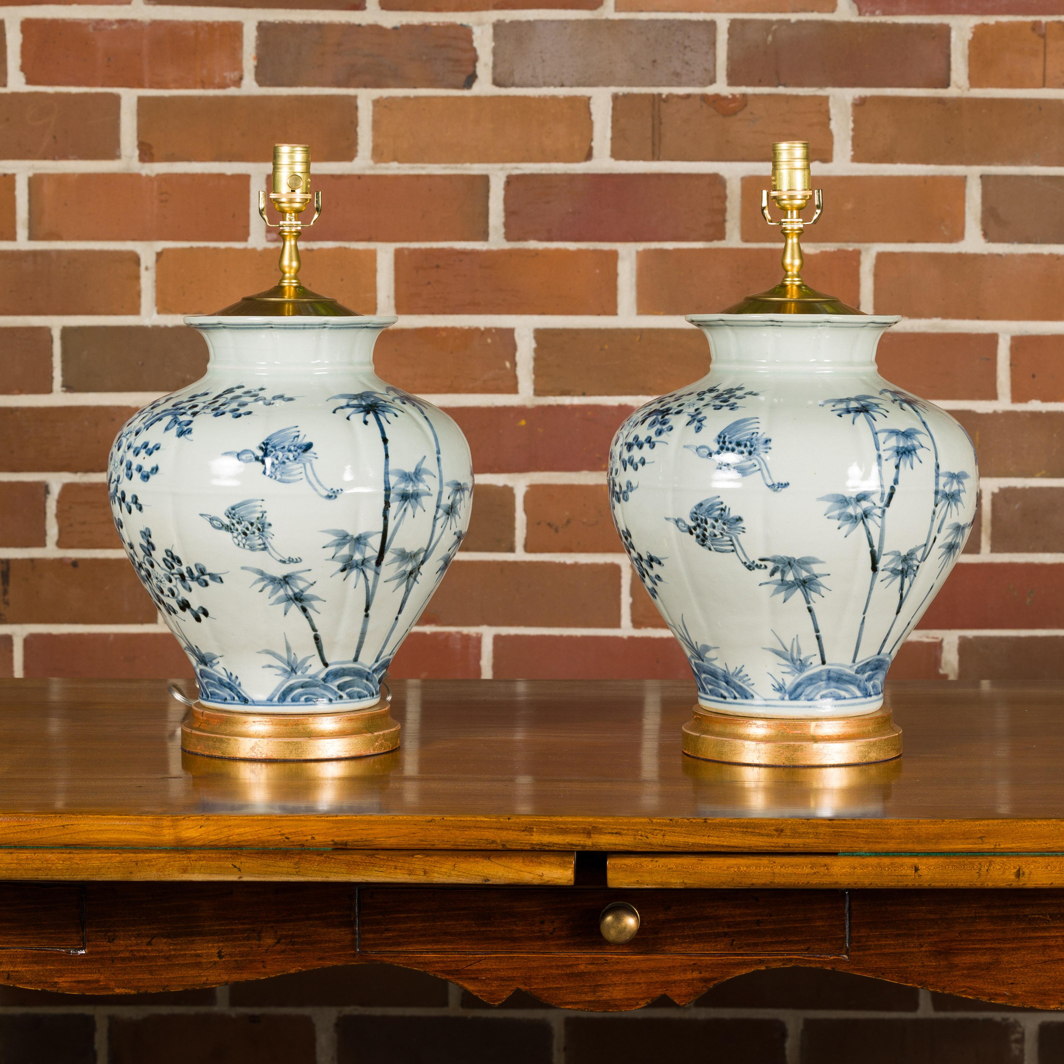 A pair of Asian blue and white porcelain vases made into single light table lamps, wired for the USA and mounted on circular giltwood bases. Elegance and artistry converge in this stunning pair of Asian blue and white porcelain vases, thoughtfully