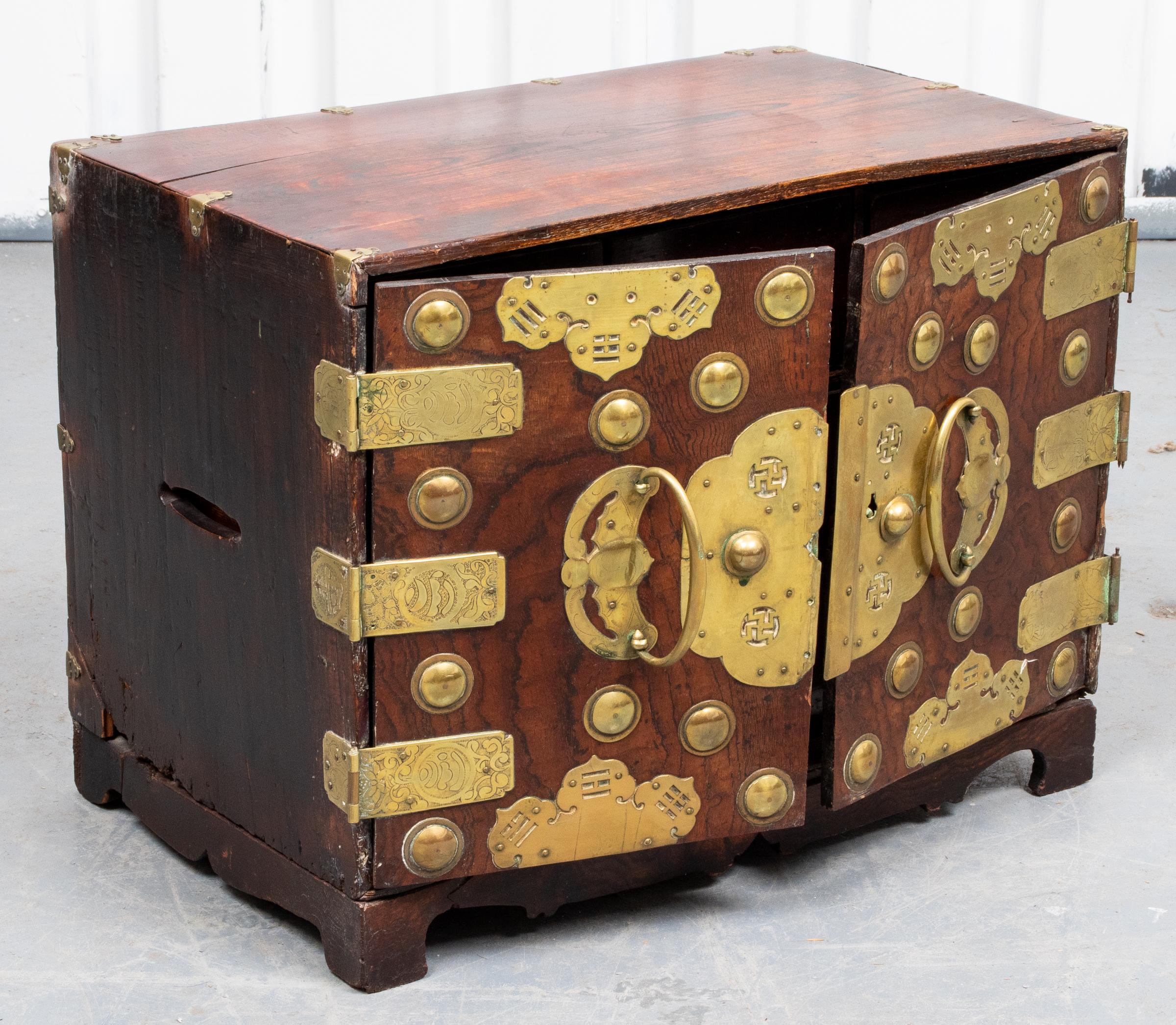Asian hardwood cabinet, overall with brass mounts etched with symbols, the doors reveal six interior drawers. Measures: 15” H x 20” W x 12.5” D.