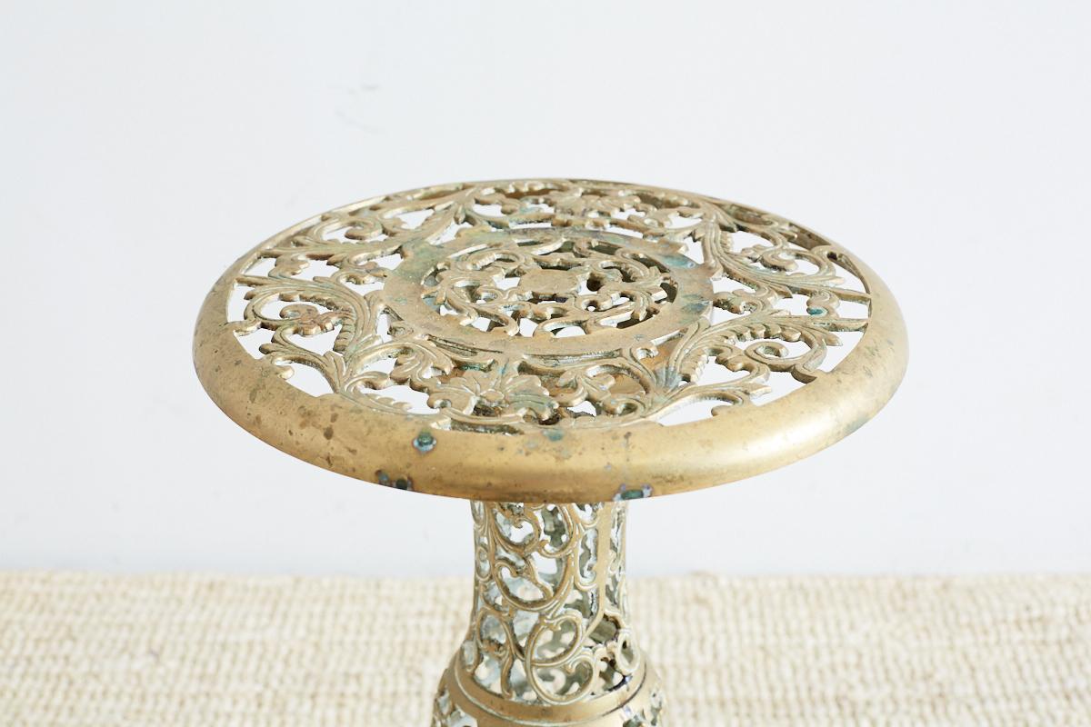 Unique Asian reticulated pedestal drinks table or plant stand. Features a pierced brass fretwork pattern of scrolling vines. Baluster form pedestal with an 11. inch round top. Lovely patinated finish with verdigris.