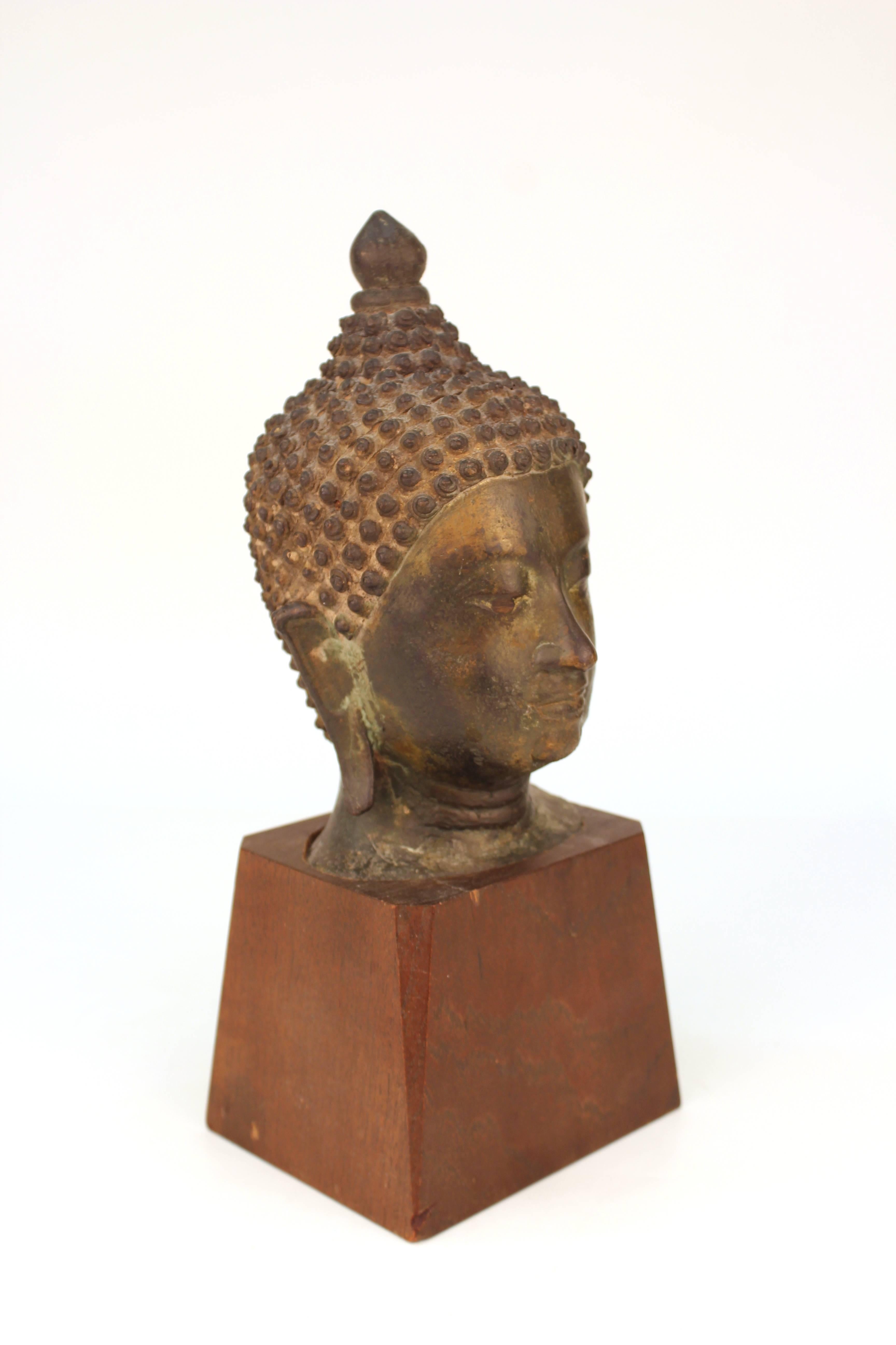 Asian black patinated bronze, depicting the head of Shakyamuni Buddha and mounted on a wooden base. There are traces of old labels on the bottom of the wood base. Some wear to patina and chips to wood base, overall in good condition.