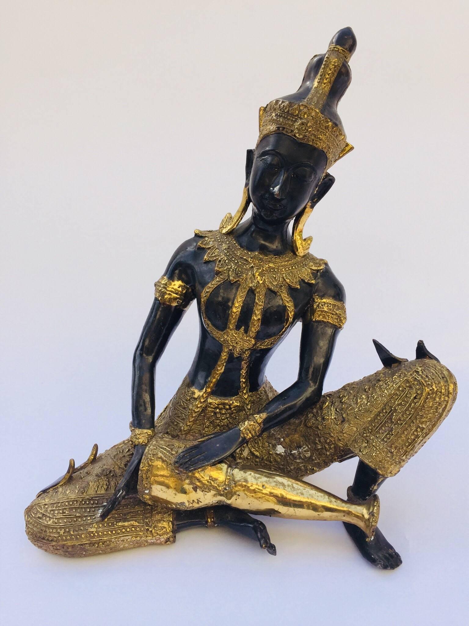 Asian bronze statue of Prince Pra Apai Manee playing a traditional Asian drum instrument. This bronze is black with the ceremonial costume and the jewelry adorned with gold leaf.
Very fine decorative Asian art work on cast bronze.
Measures: Height