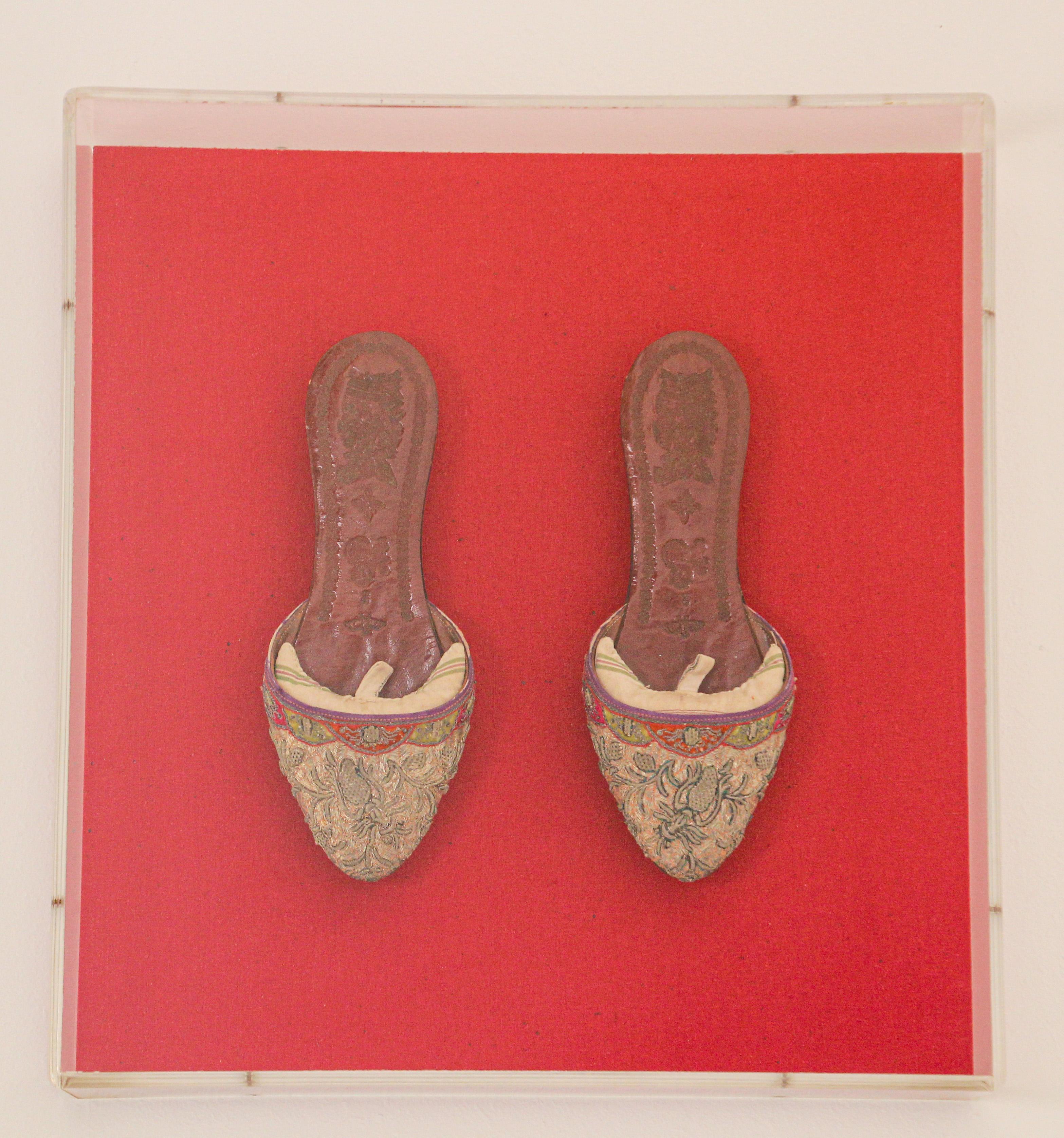 Framed in a Lucite box, pair of Asian Chinese leather and silk shoes embroidered and adorned with gold thread.
Exquisite pair of collectible antique shoes mounted and presented on a red background.
Great Asian framed Textile Collectible Wall Art.