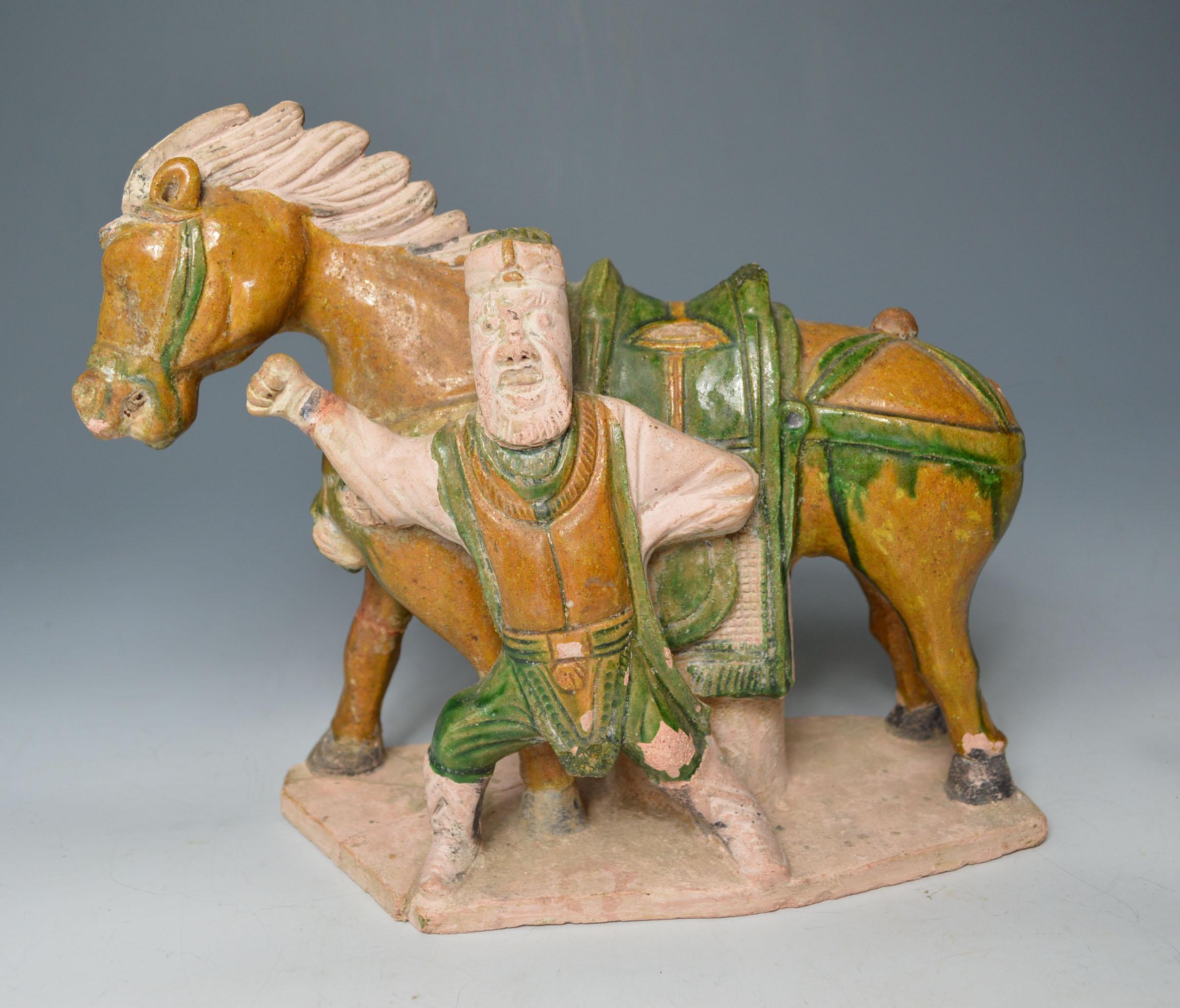 A Ming dynasty figure of a horse with standing warrior
The pottery figure of a horse with standing bearded warrior with outstretched arm
On a rectangular base the pottery glazed in green and brown.
Ming dynasty (1368-1644 CE). 
Dimensions: W 28