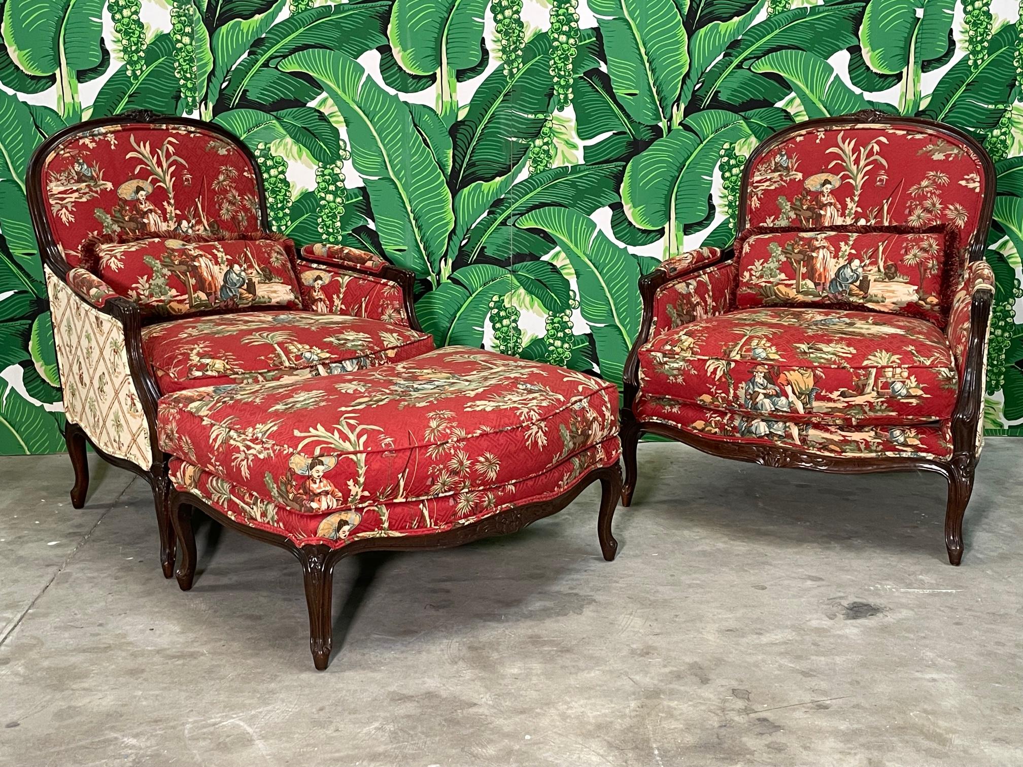 Pair of Bergere chairs with matching ottoman feature a chinoiserie fabric, cabriole legs, and hand carved detailing on the frame. Very good condition with only minor imperfections consistent with age. As with all vintage pieces, may exhibit scuffs,