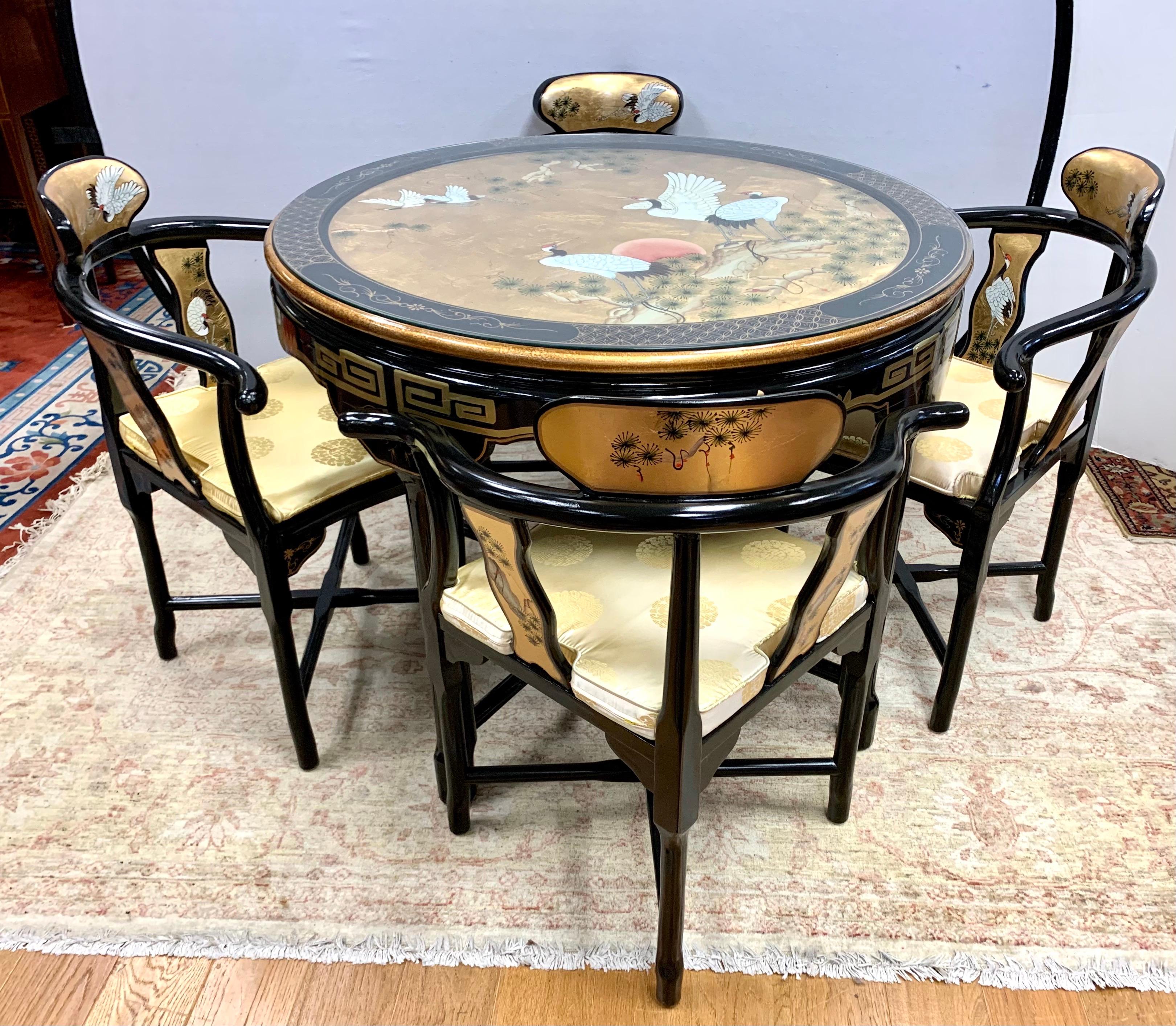 Stunning Chinese black lacquered set includes a table with 4 chairs and features a hand painted motif of cranes and flowers on a gold gilt background. The table top also has a Greek key design in gold on the carved apron. Each chair is painted on