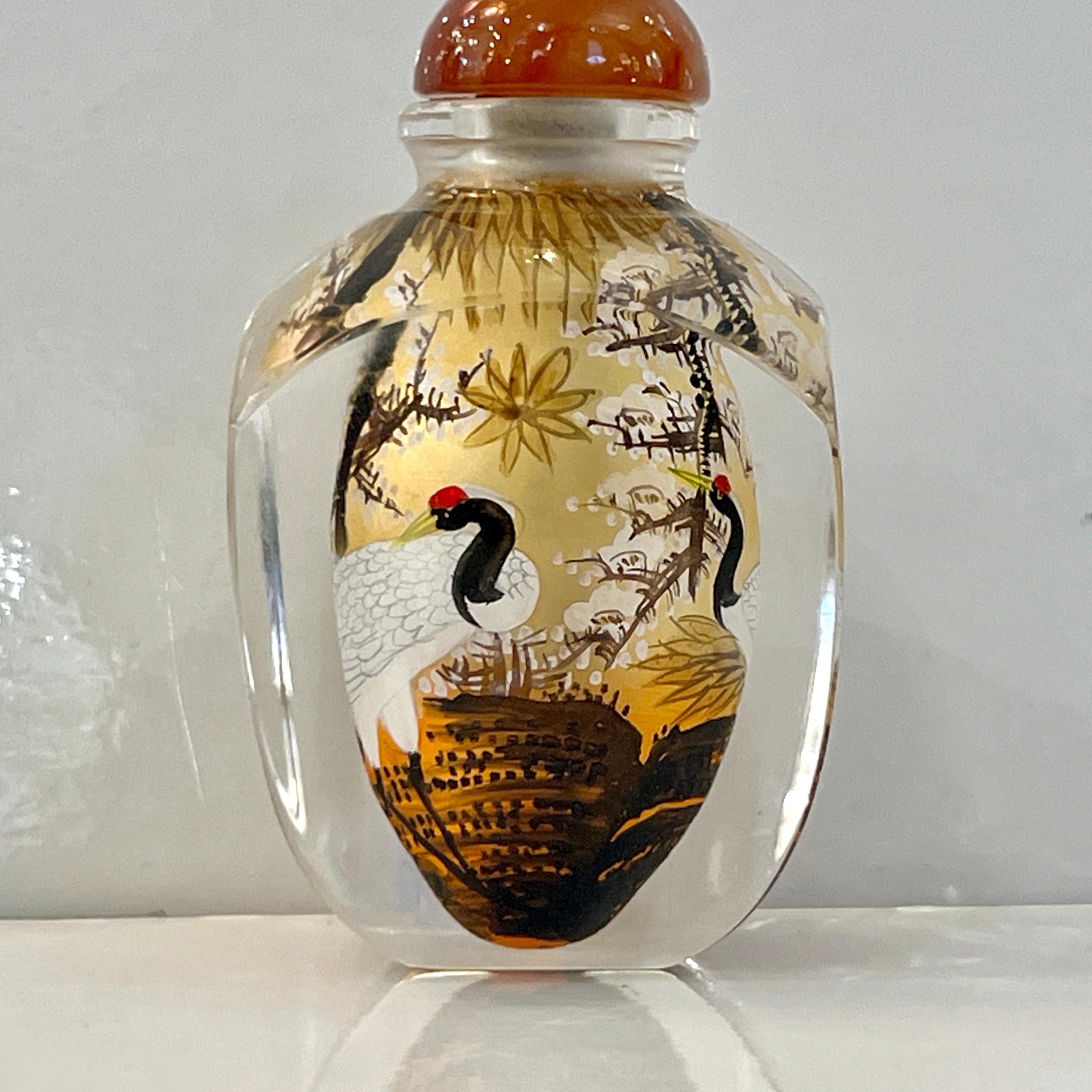 A delightful églomisé reverse-painted Chinese decorative snuff bottle, with a captivating scene depicting a landscape with white blossom trees and red-crowned white and black cranes delicately free hand painted in the foreground, with symbolic