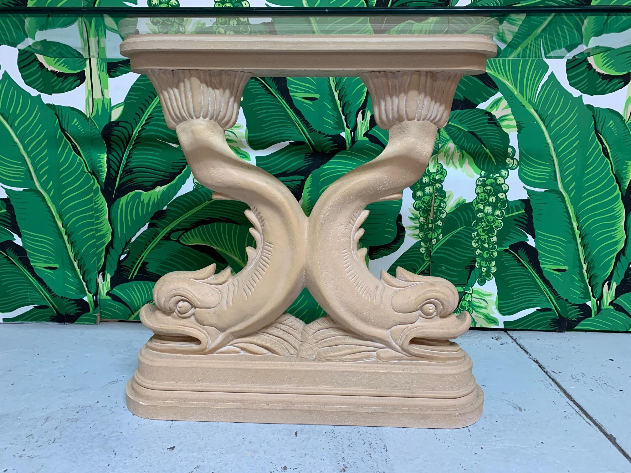 Sculptural chinoiserie console table features a pedestal of twin Asian dolphins holding a beveled glass top. Cast plaster base. Very good vintage condition with very minor imperfections consistent with age. Glass measures 46