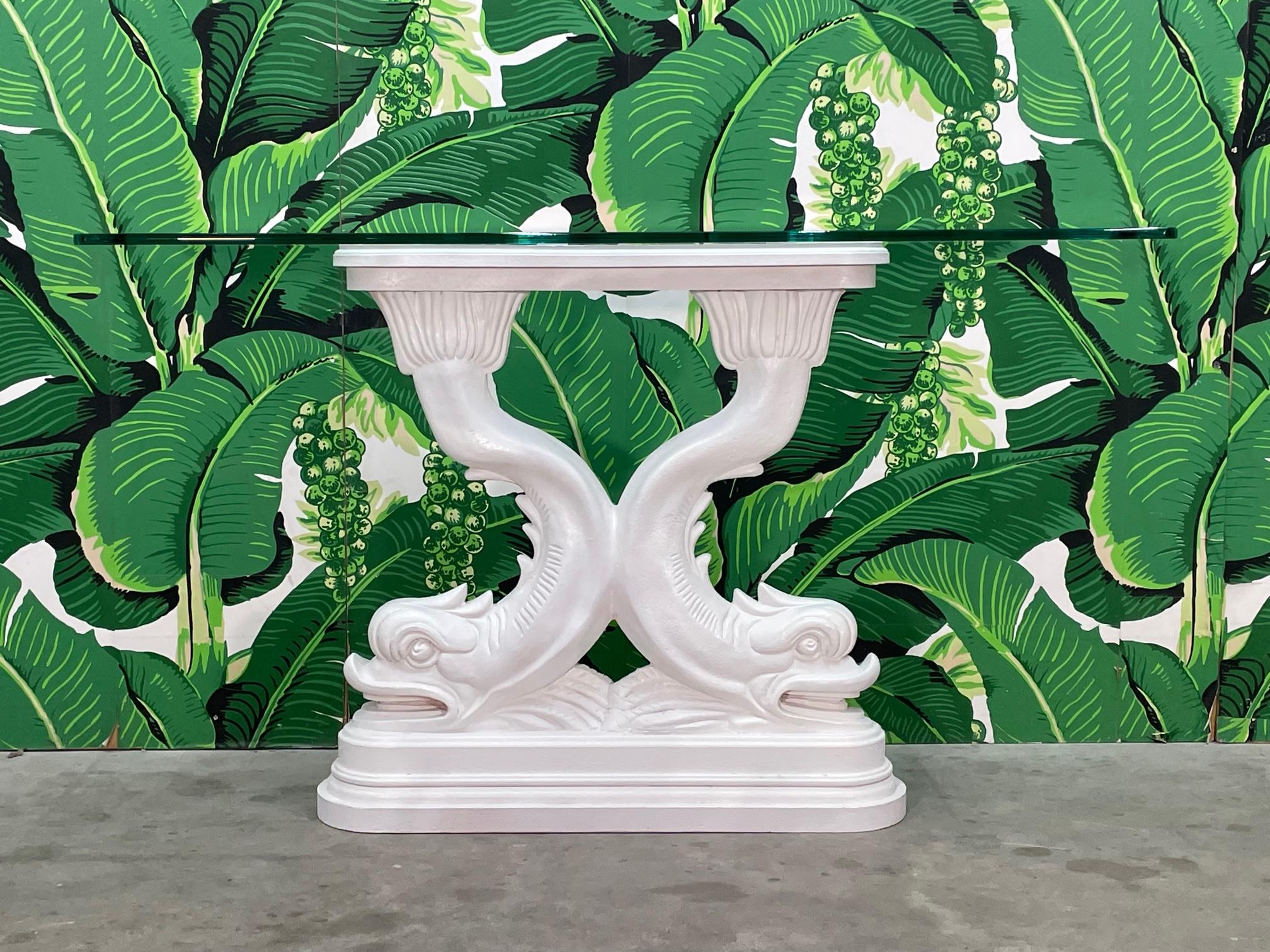 Sculptural Chinoiserie style console table features a pedestal of twin Asian dolphins under a glass top. Cast plaster base. Base has been recently refinished in gloss white. Good condition with minor imperfections consistent with age, see photos for
