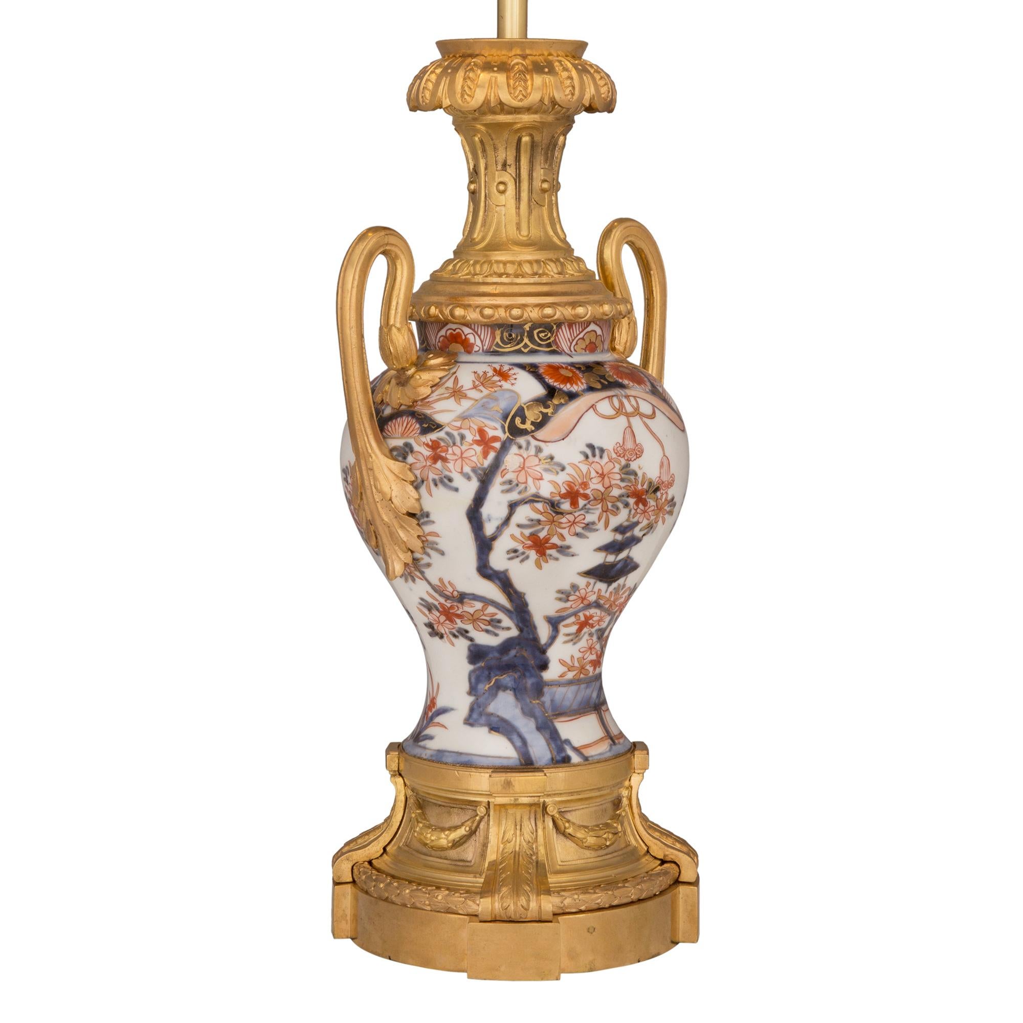Une belle lampe de grande qualité en porcelaine et bronze doré de style Louis XVI du 19ème siècle, de collaboration entre l'Asie et la France. La lampe est surélevée par une élégante base en bronze doré, ornée de fines guirlandes de laurier et