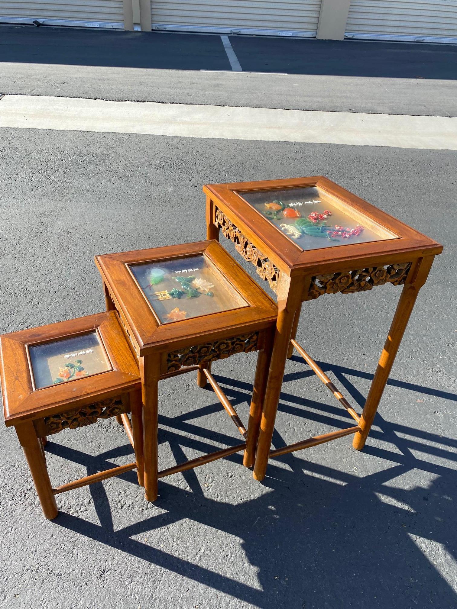 Set of three Chinese nesting tables / stacking tables. Each featuring hand carved design and showcased glass tops featuring auspicious items and character crafted of semi-precious stones on each table. This set is extremely unique. Dimensions from