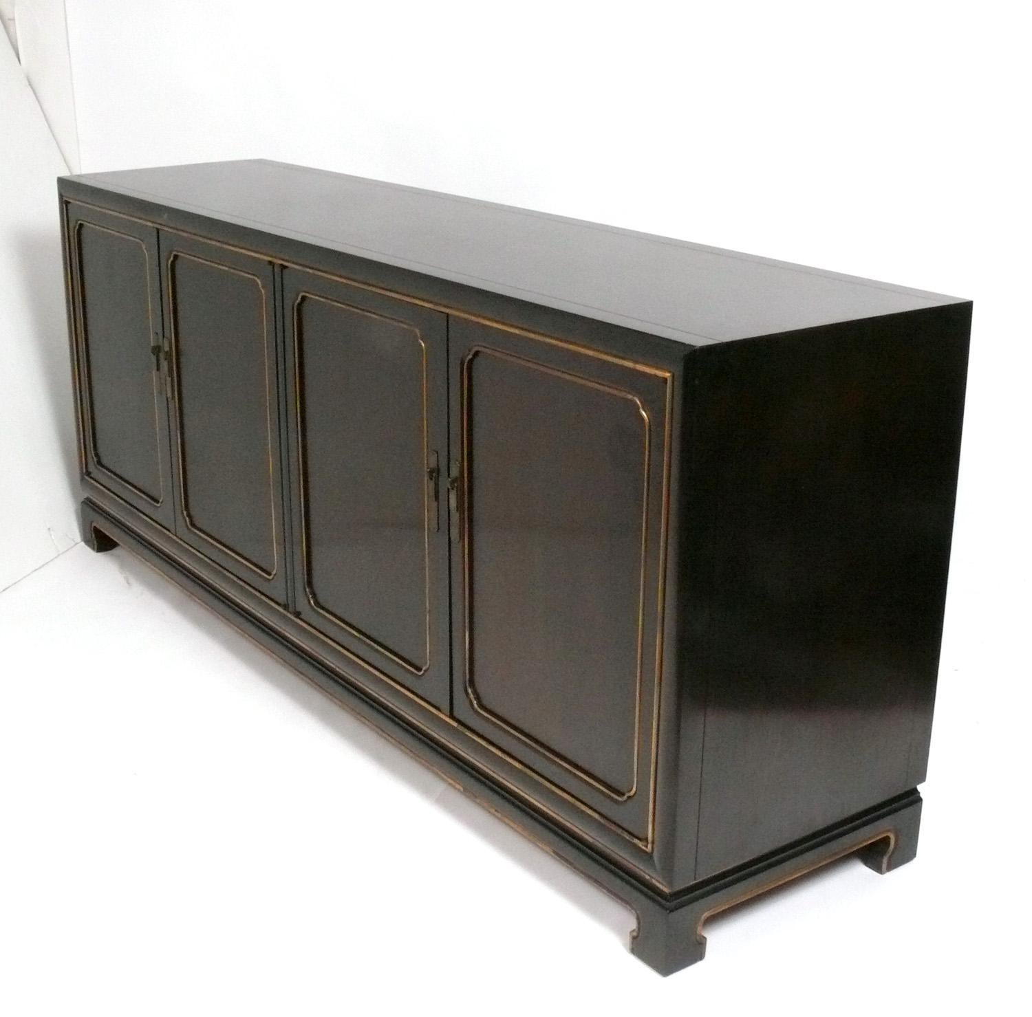 Asian Influenced Mid Century Credenza, designed for the John Widdicomb Company, American, circa 1960s. Subtle Asian influenced design executed in a deep espresso brown color with gold trim and patinated brass hardware. It offers a voluminous amount