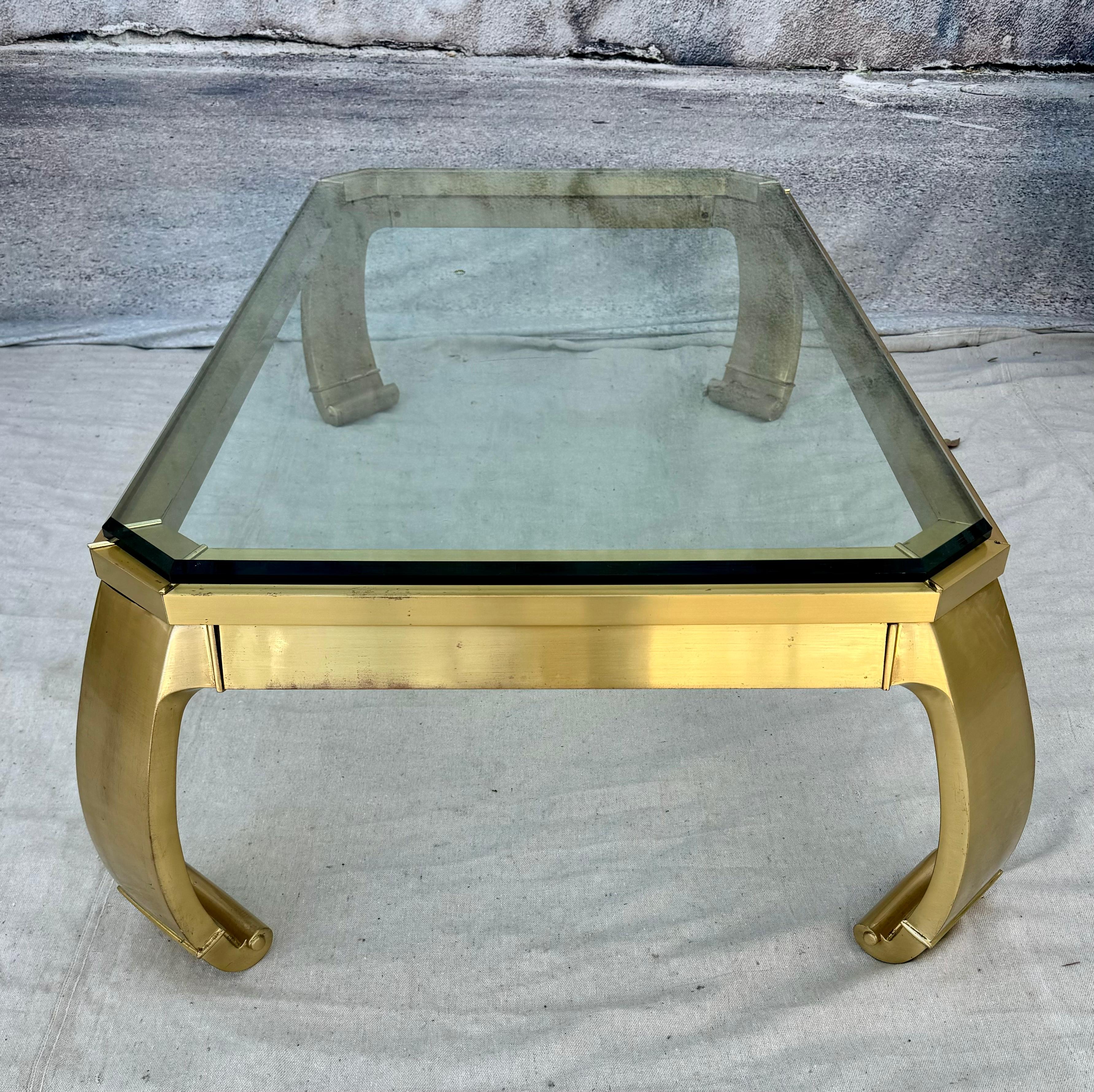 This 1960's vintage rectangular Asian coffee table is in the iconic Mastercraft style, and features a brass frame with rounded legs with scrolled toes. Heavy beveled glass sits on top. This elegant coffee table radiates grace and sophistication.