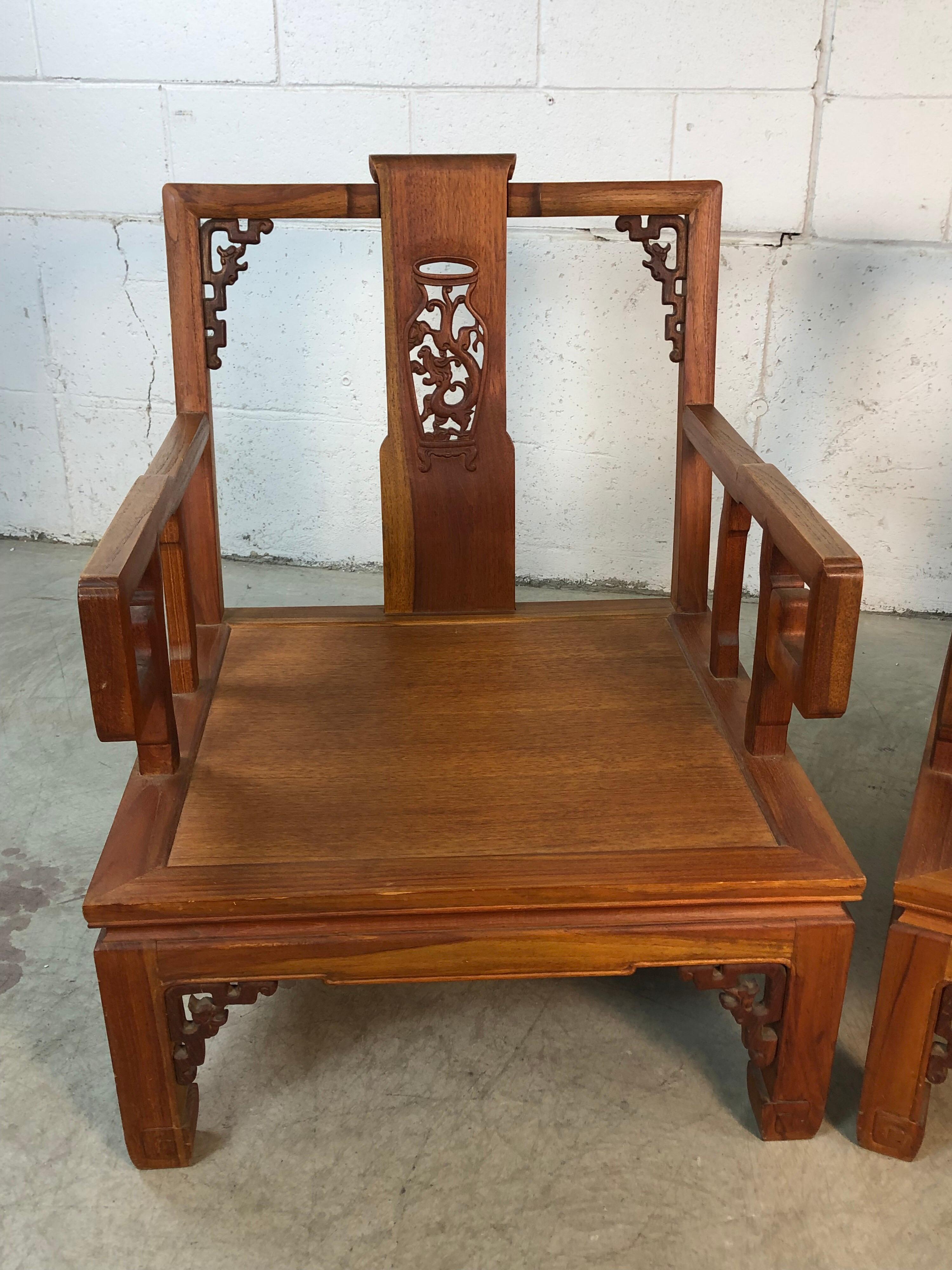 Vintage pair of Asian Ming style low hand carved wood armchairs. The chairs have dragon carved accents and are sturdy heavy solid wood chairs. The dragon accents run along the backs and skirts of the chairs. The chairs will come with the original
