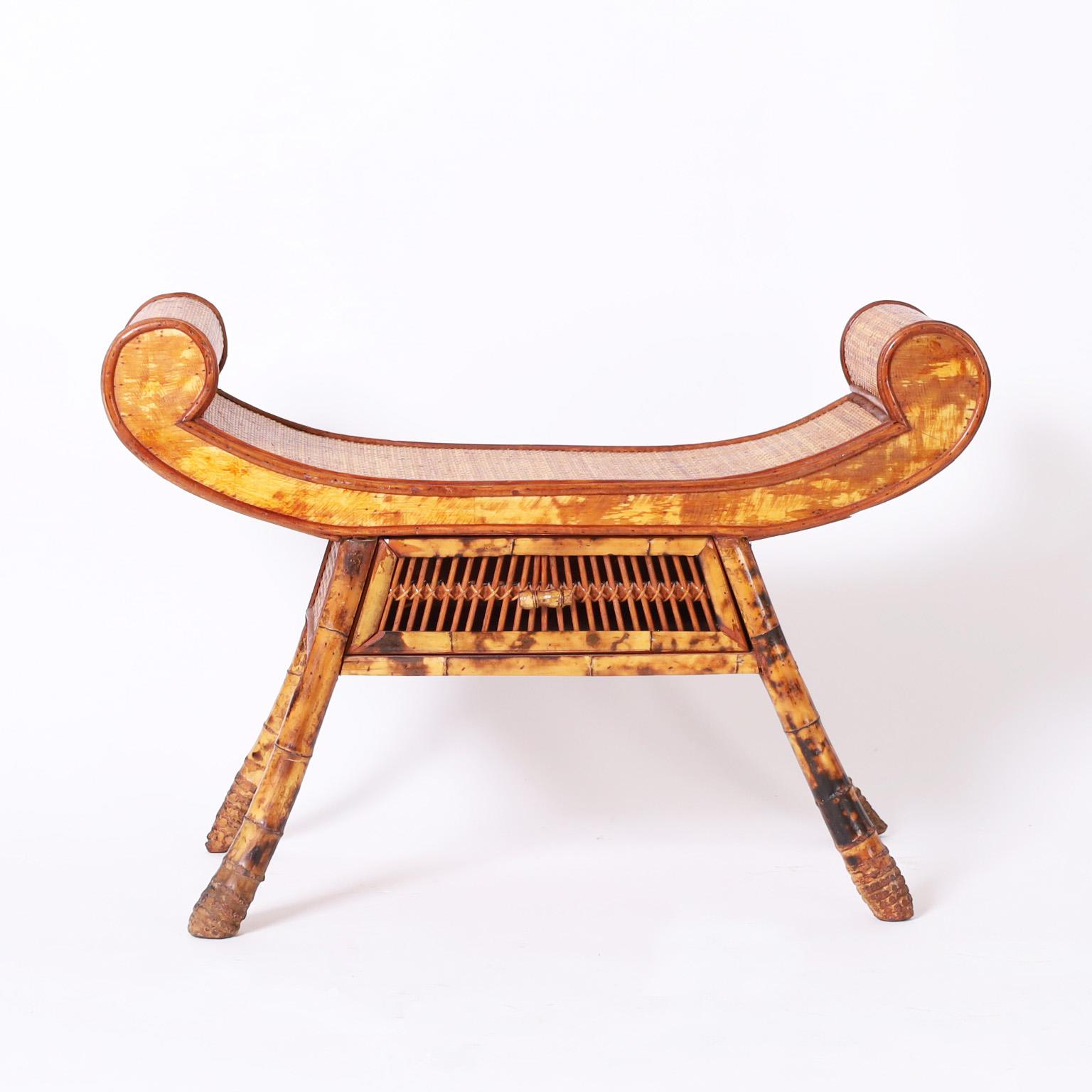 Midcentury Asian style bench having an elegant rolled seat covered in grasscloth bordered with rattan over a case with a drawer on burnt bamboo legs with root feet.