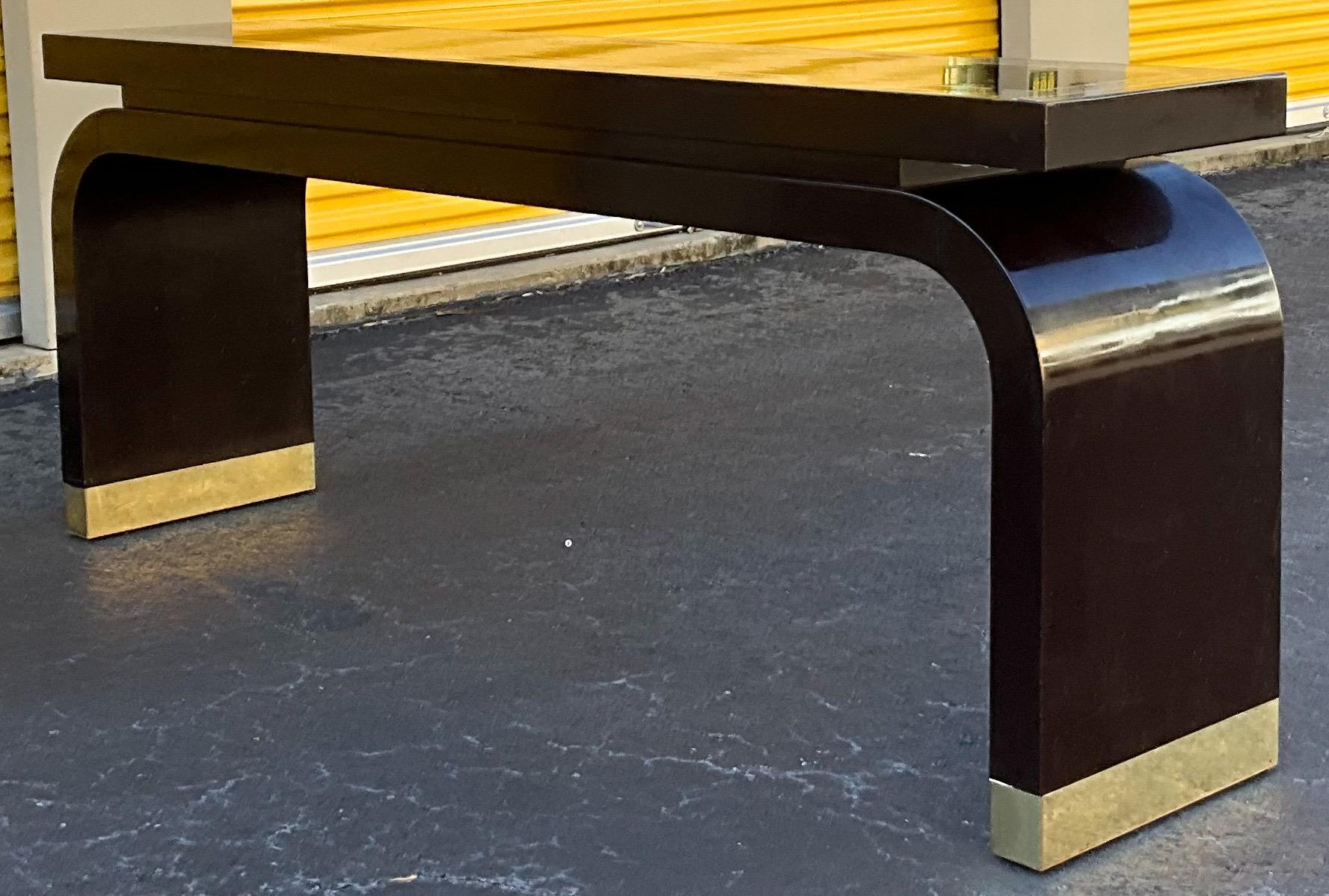 This is a sleek modern Ming style console table by Baker Furniture Company. The piece has an espresso finish with a high gloss clear coat. The top has a faux marble painted inset stripe. The base has brass caps that show some wear. It is marked.