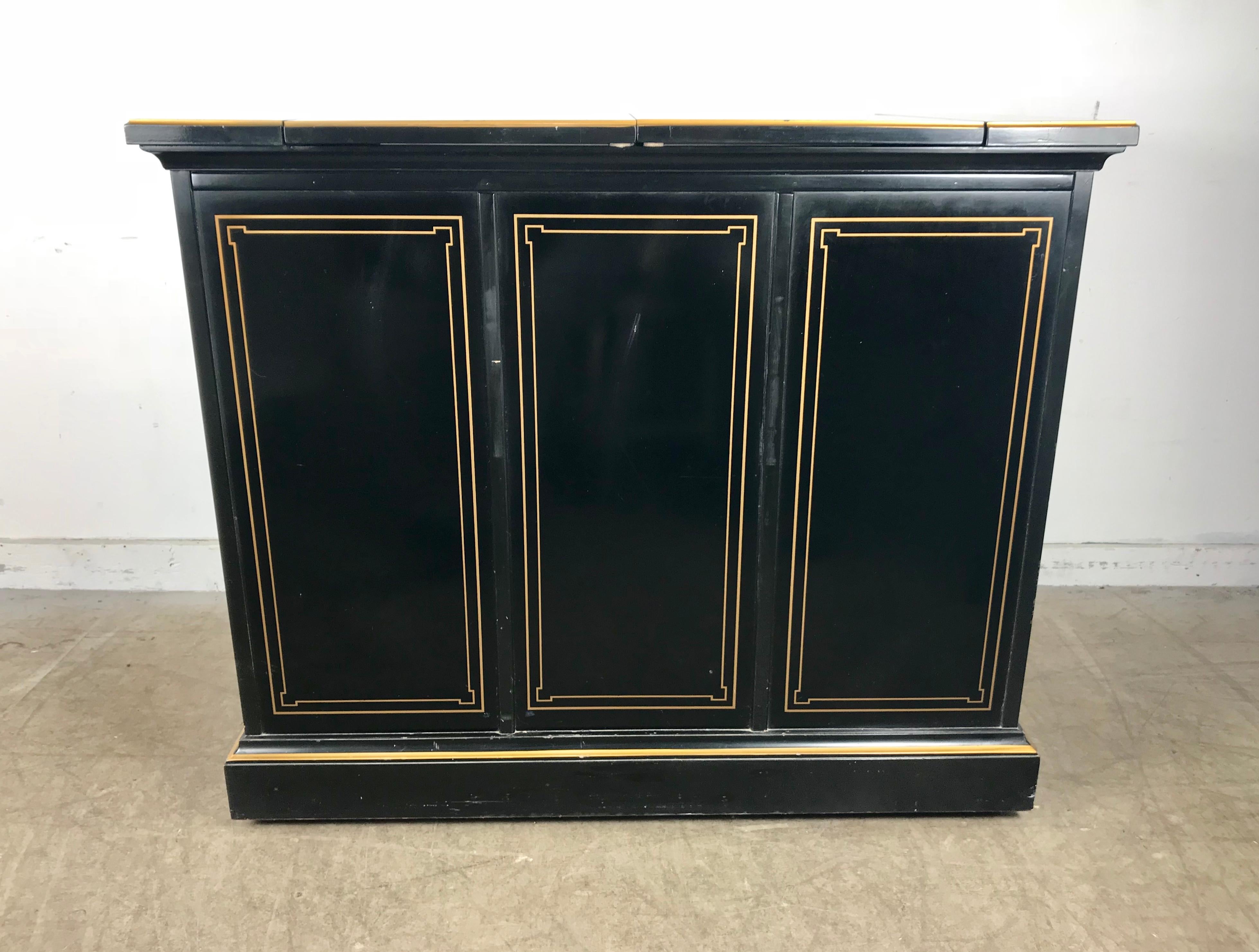 Asian modern rolling bar cabinet by Drexel, black lacquer dry bar/liquor cabinet is decorated with gold gilt trim and hand painted details, including scenes of people in natural settings, pagodas, and flowers.
Top folds out to nearly double the