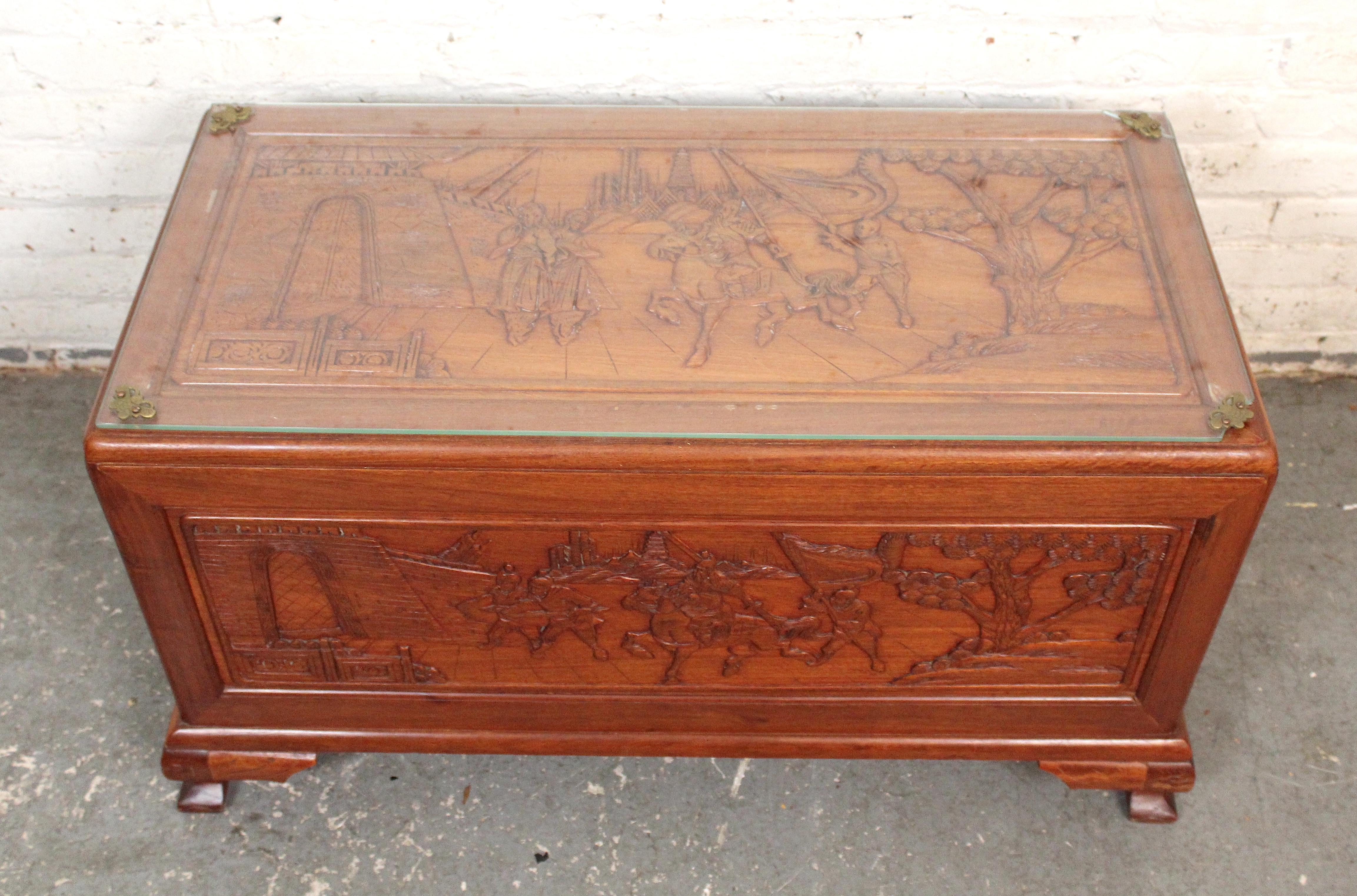 This highly carved table is detailed on all sides, and designed as a storage trunk, but functions as a glass top coffee table. The intricate detailed engraved scenes are on the front, back and top, while the sides boast two drawers for