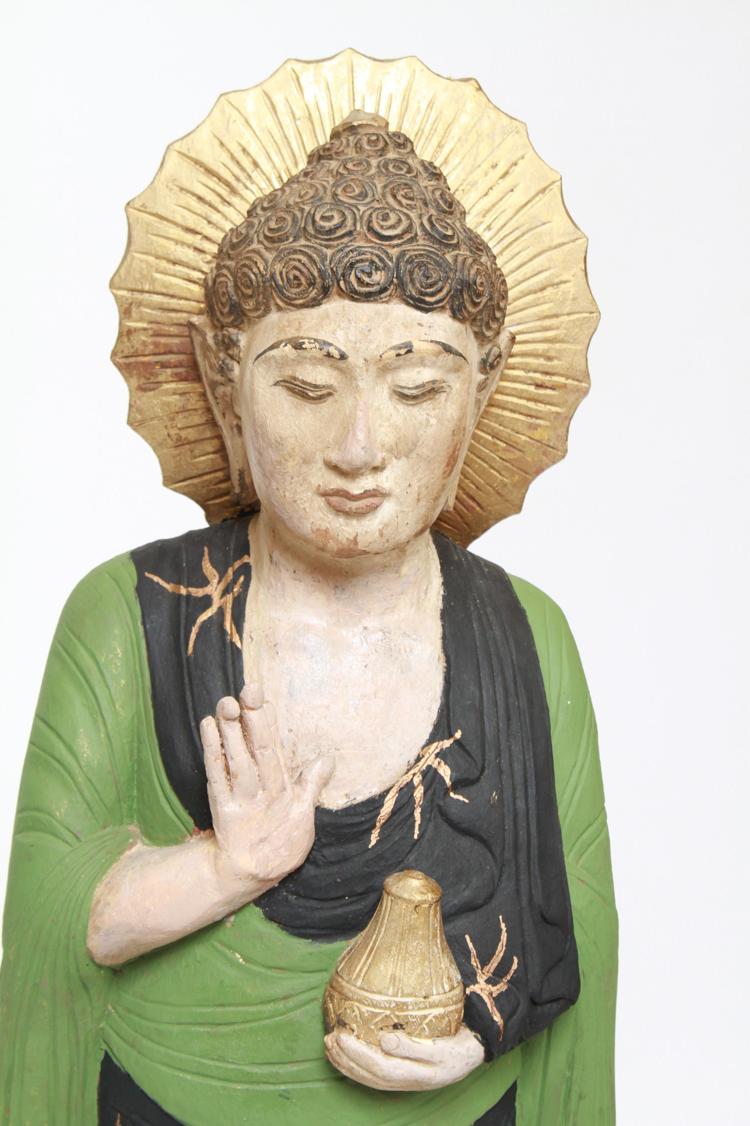 Asian polychrome statue of a standing Guanyin, molded, with right hand pointed upwards and his left hand holding a medicine bottle, the head framed by a golden halo and wearing a green and black garment. In great vintage condition.
